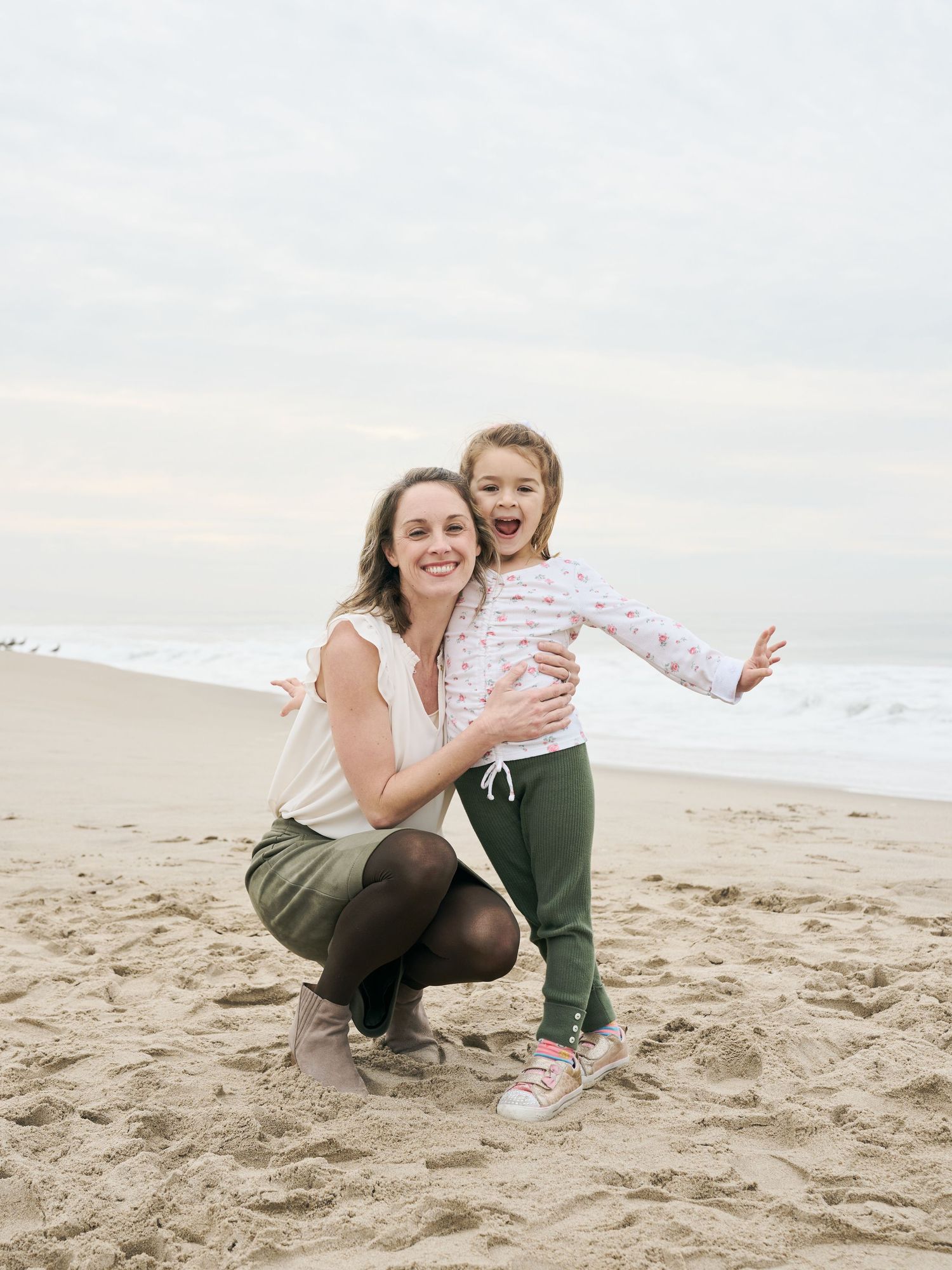 A joyful moment captured between two people embracing and laughing together on a cloudy beach.