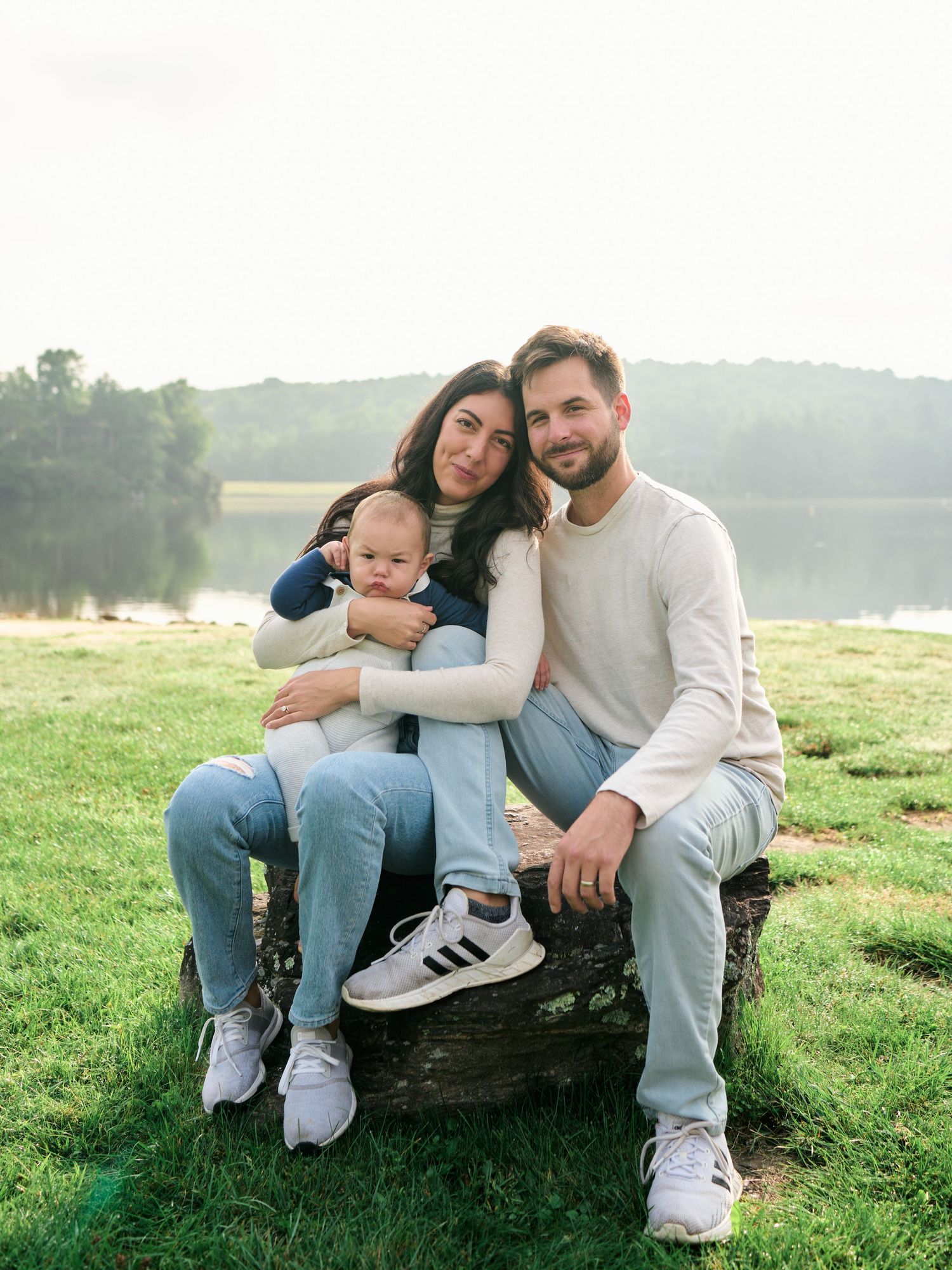 A family sits together on a rustic log bench by a serene lake on a misty morning.