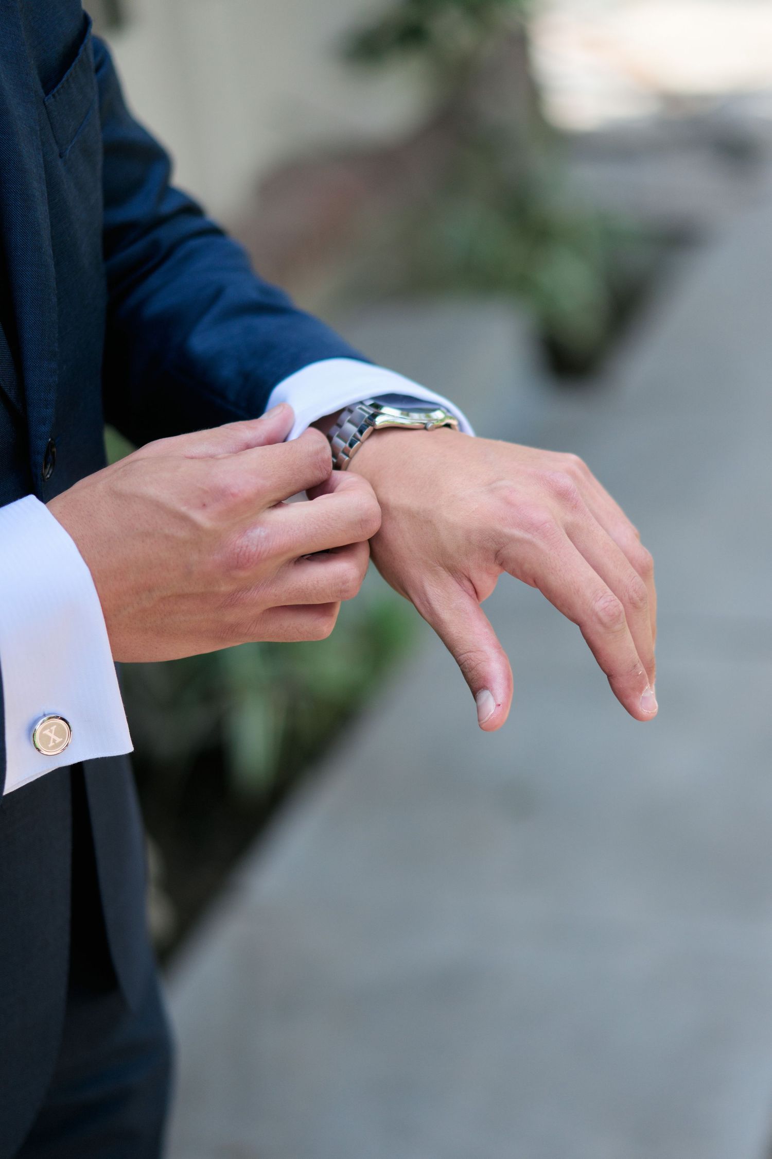 Close-up shot of hands adjusting a watch with a navy suit sleeve and white cuff visible.