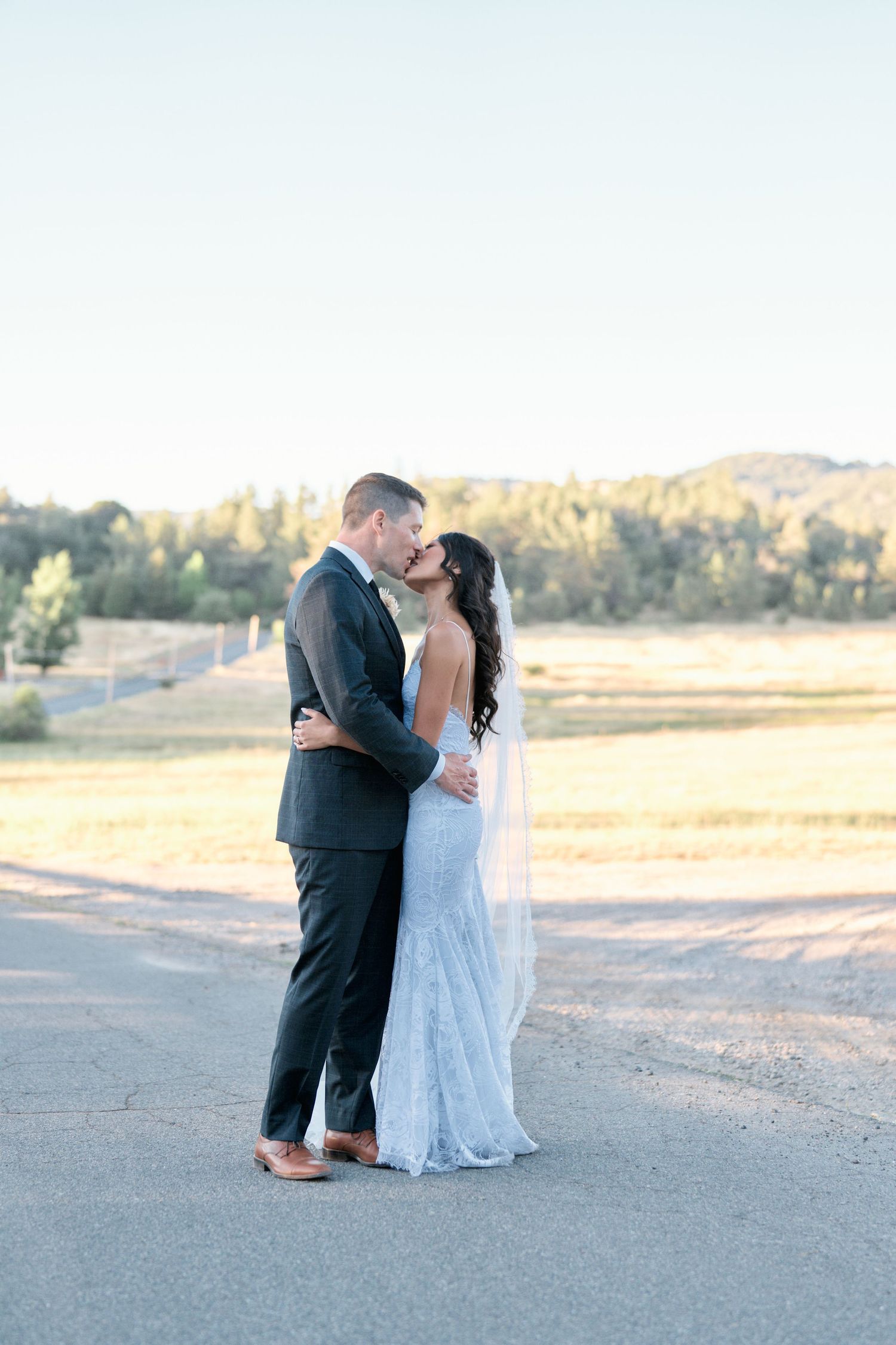 A romantic moment captured at sunset in an open field with mountains in the background.