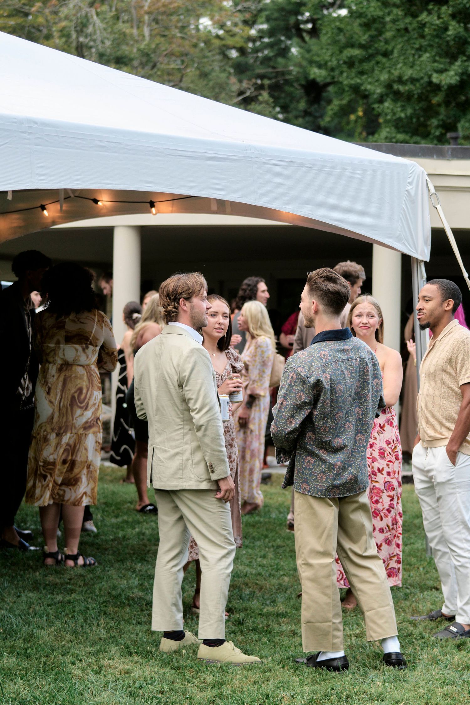 Guests mingle under a white tent during an outdoor wedding reception.