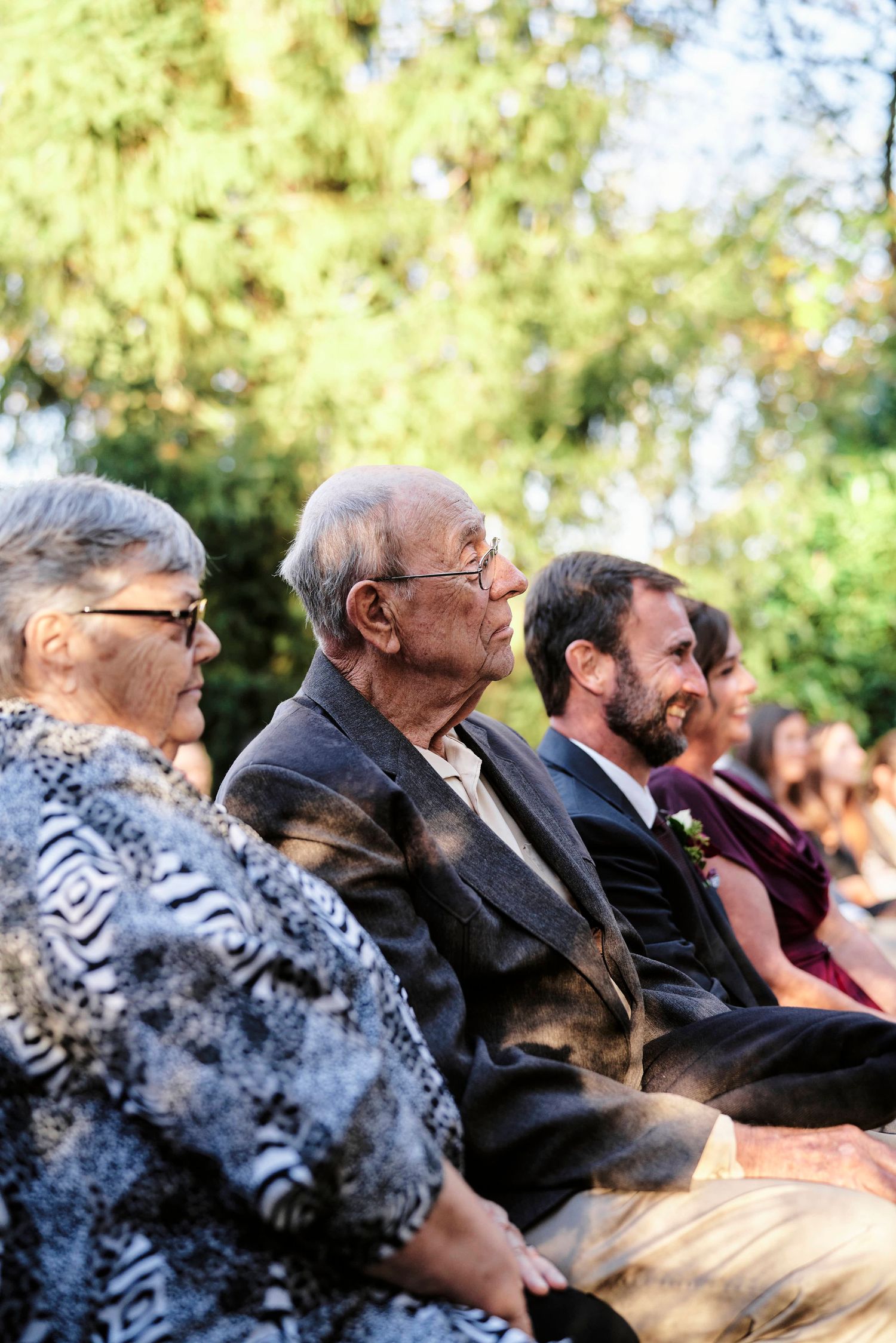 Wedding guests watching ceremony intently from outdoor seating area.