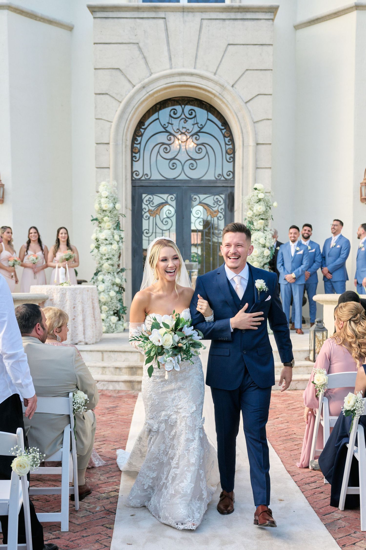 Wedding ceremony recessional at elegant venue with ornate iron door and white floral decorations.