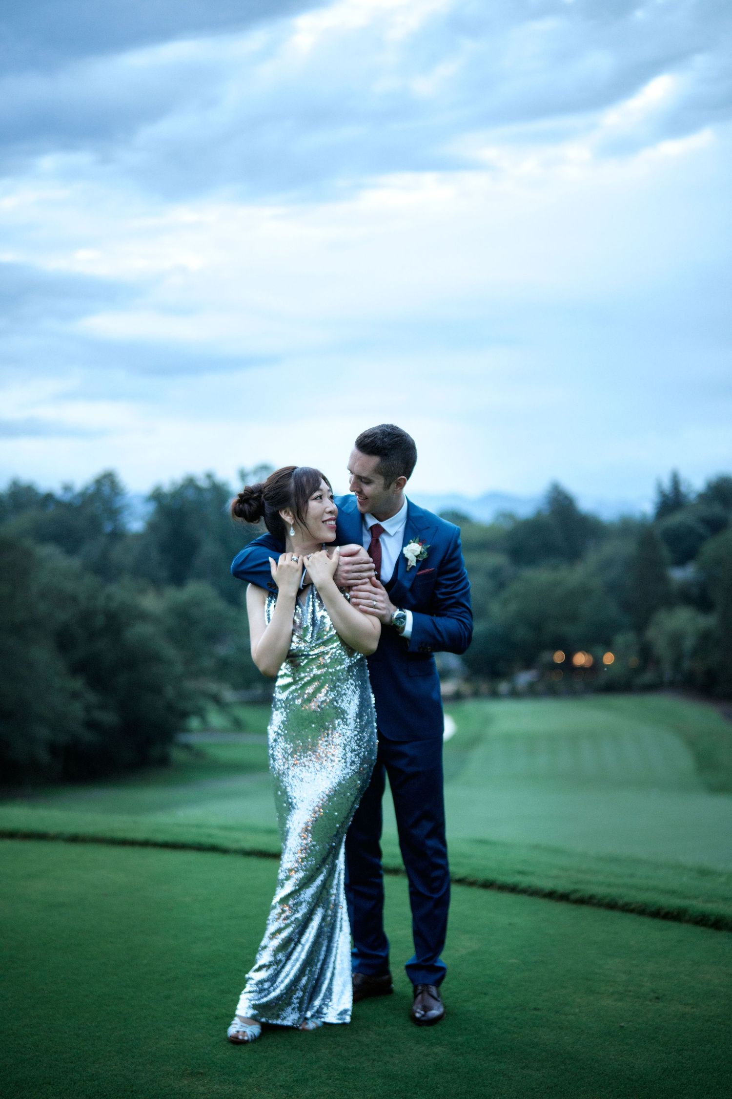 A couple in elegant attire shares a dance on a manicured golf course under blue evening skies.