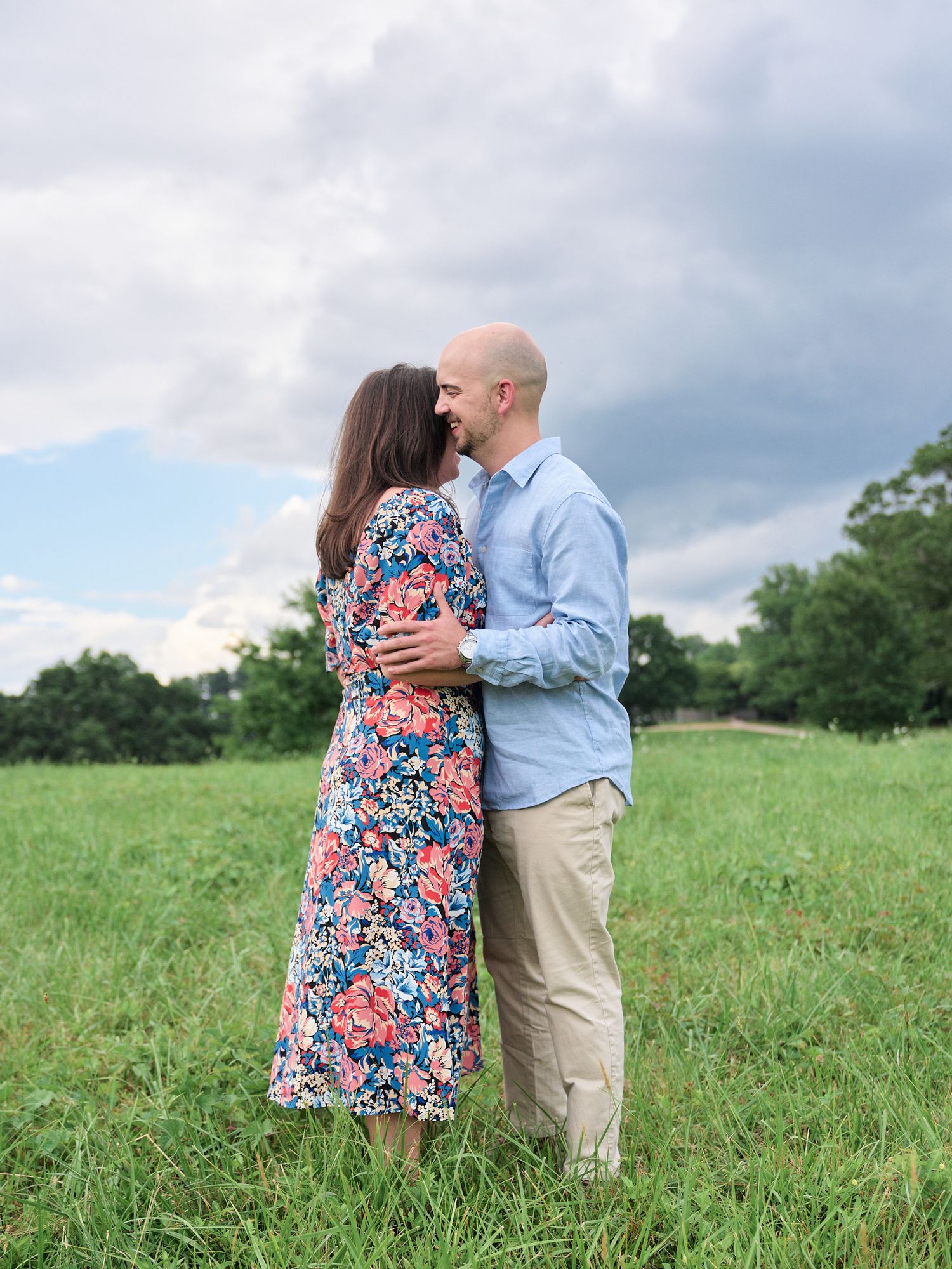 Romantic couple embraces in a sunlit meadow with mountains in background.