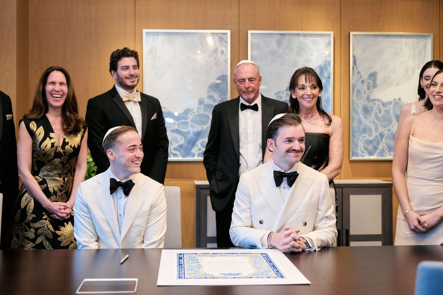Wedding ceremony participants gather in formal attire for document signing in an office setting.