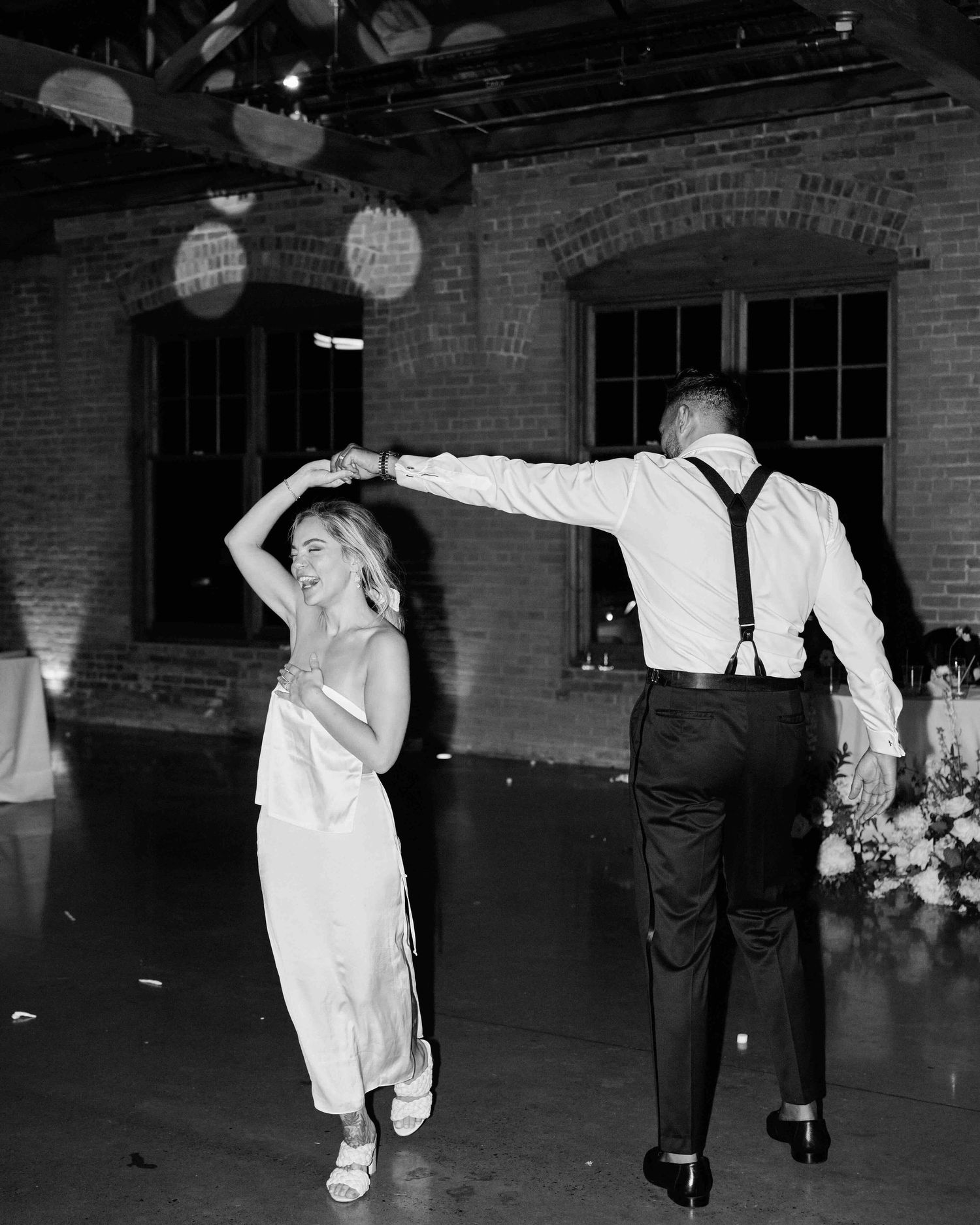 Black and white photo of bride and groom dancing at wedding reception in rustic brick venue.
