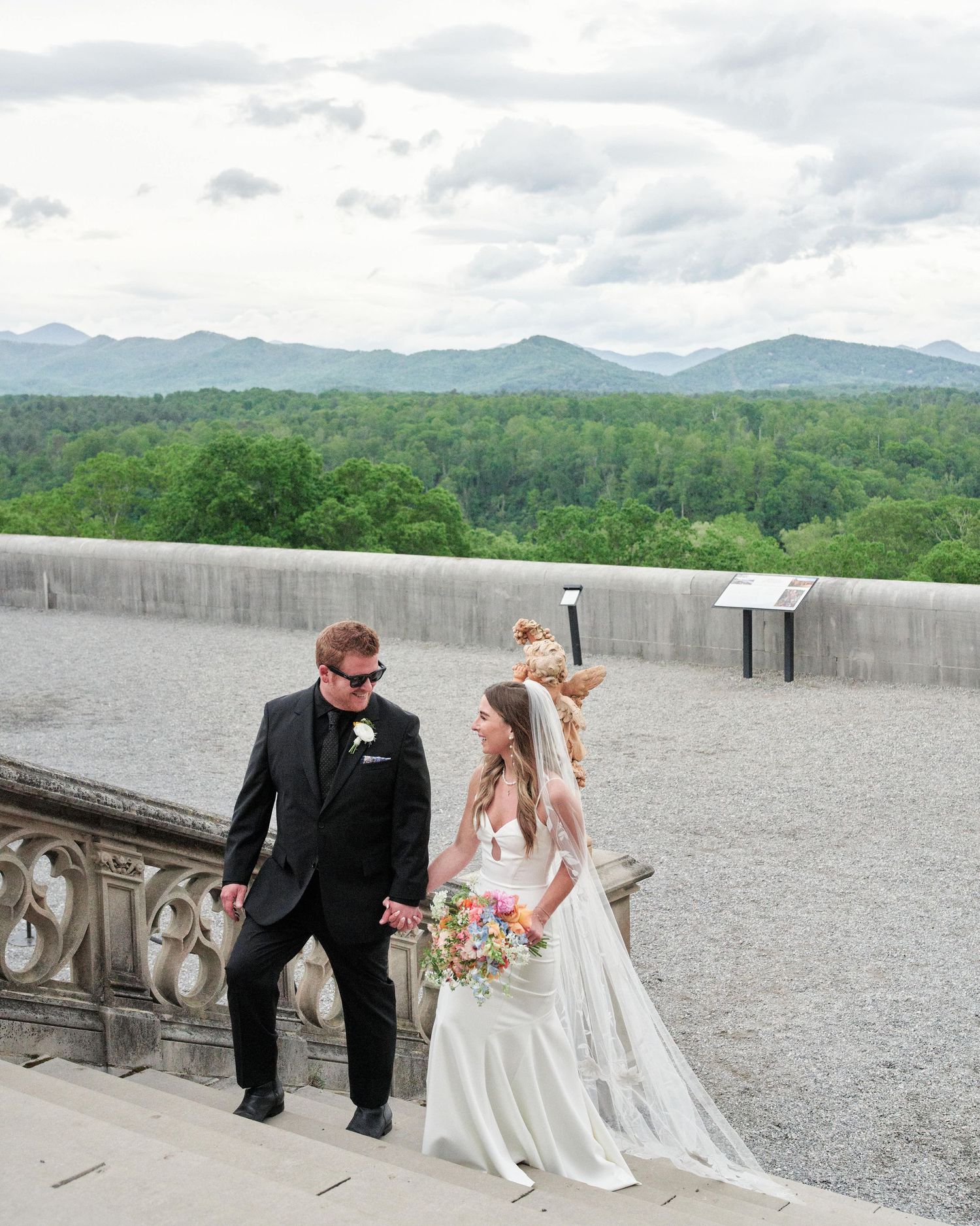 A wedding couple shares intimate moments along a stone balcony overlooking mountain views at Biltmore Estate.