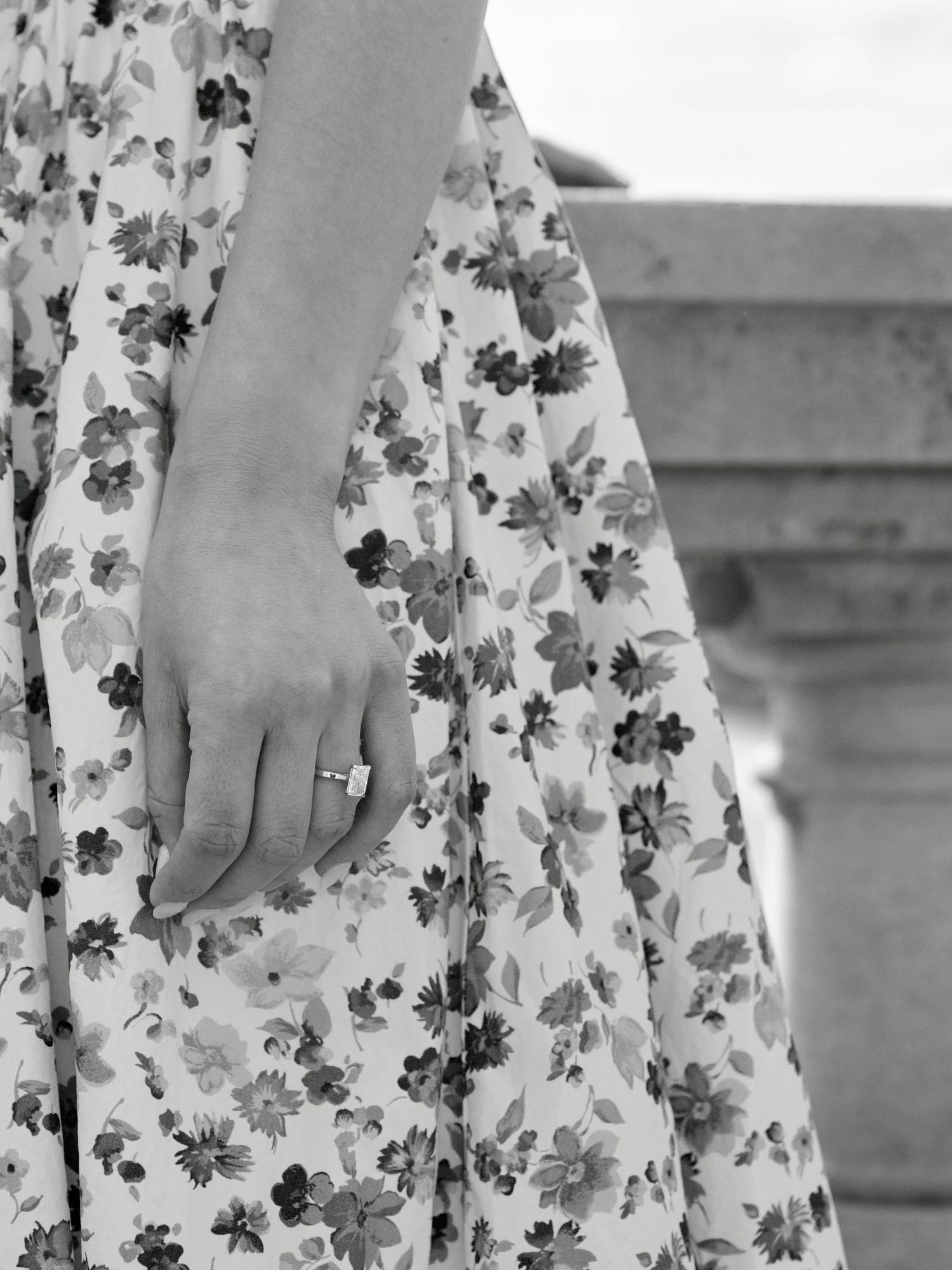 Close-up of a woman's hand with an engagement ring resting on a floral dress.