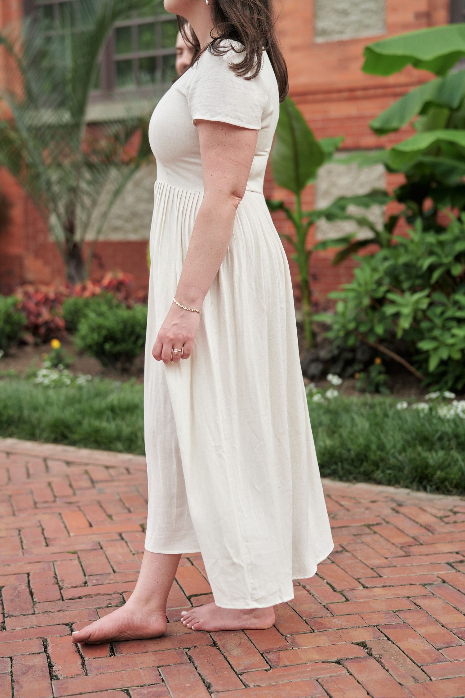 A cream-colored maxi dress with short sleeves shown on brick pavement.