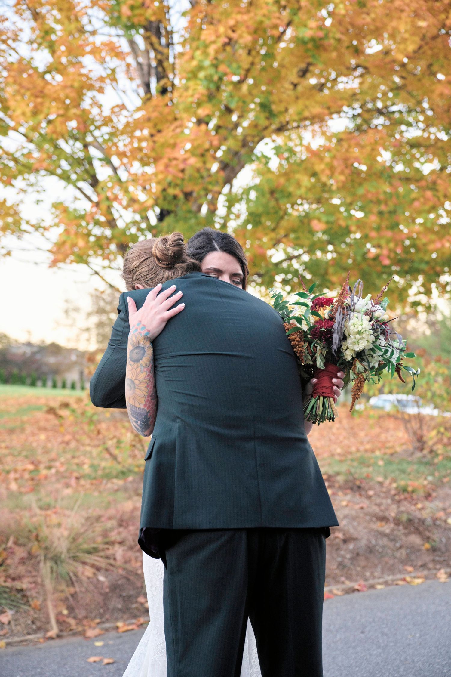 A couple shares an intimate embrace while holding a fall wedding bouquet.