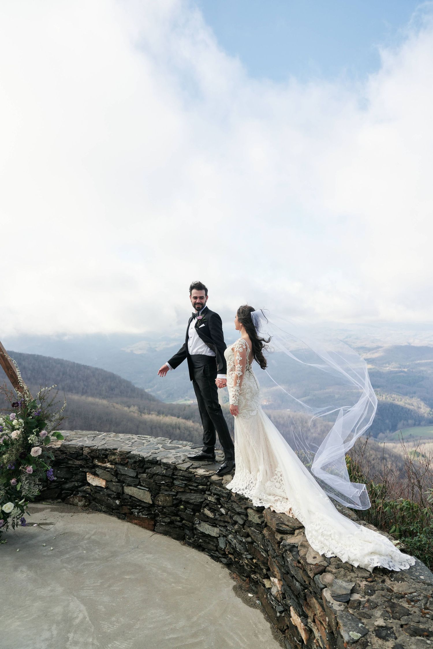 groom holding the brides hand as they are walking a top the mountain with the smokey mountains in the background