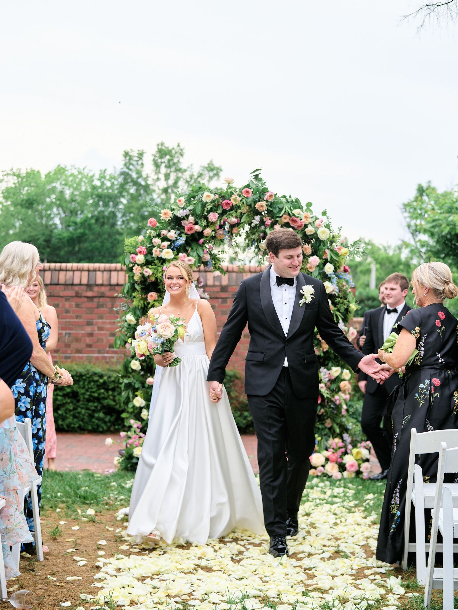 Newlyweds walking down the aisle on rose petals after outdoor garden ceremony.