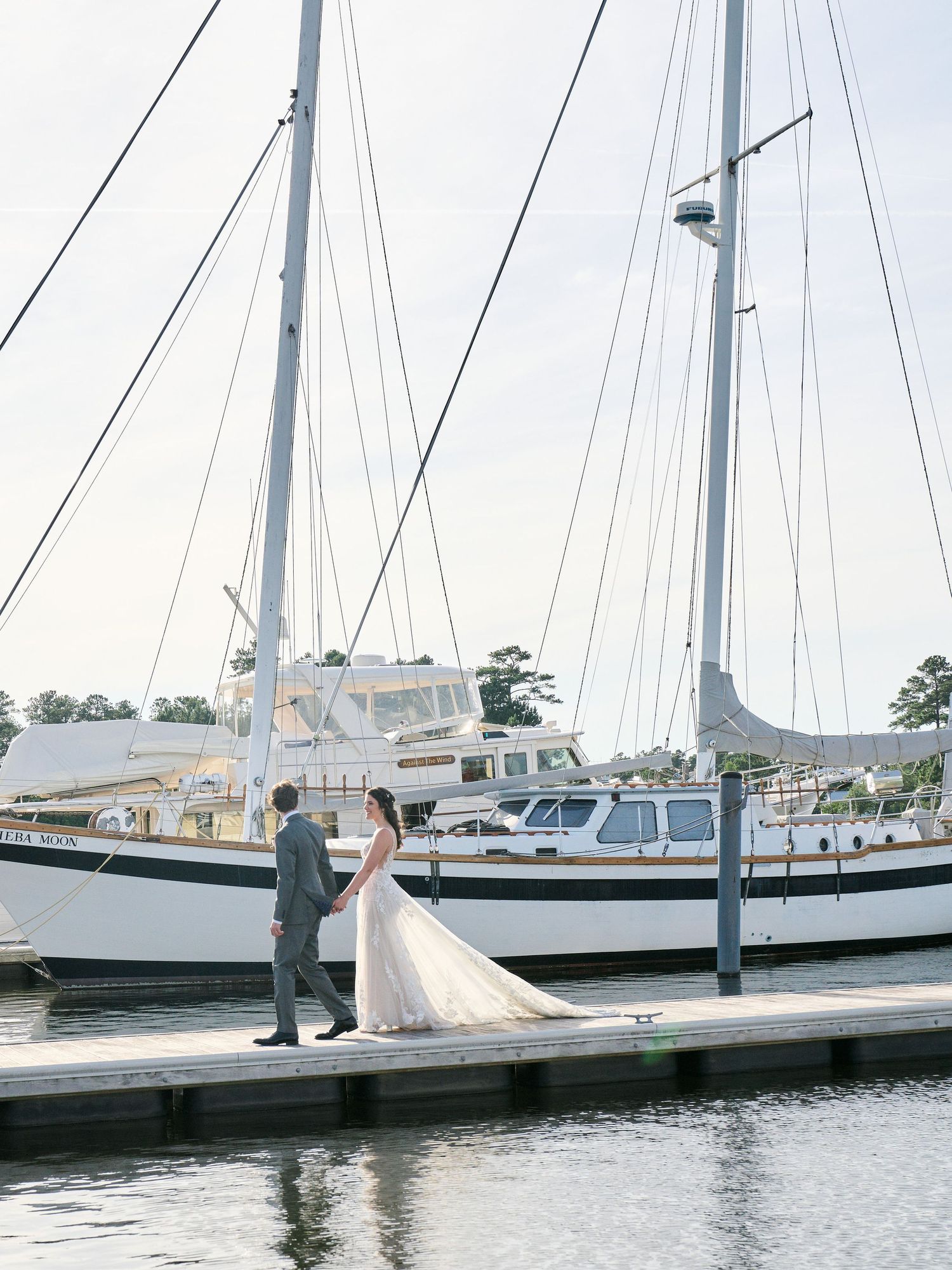 Romantic couple standing together on a boat dock beside sailing yachts at a marina on a bright day.