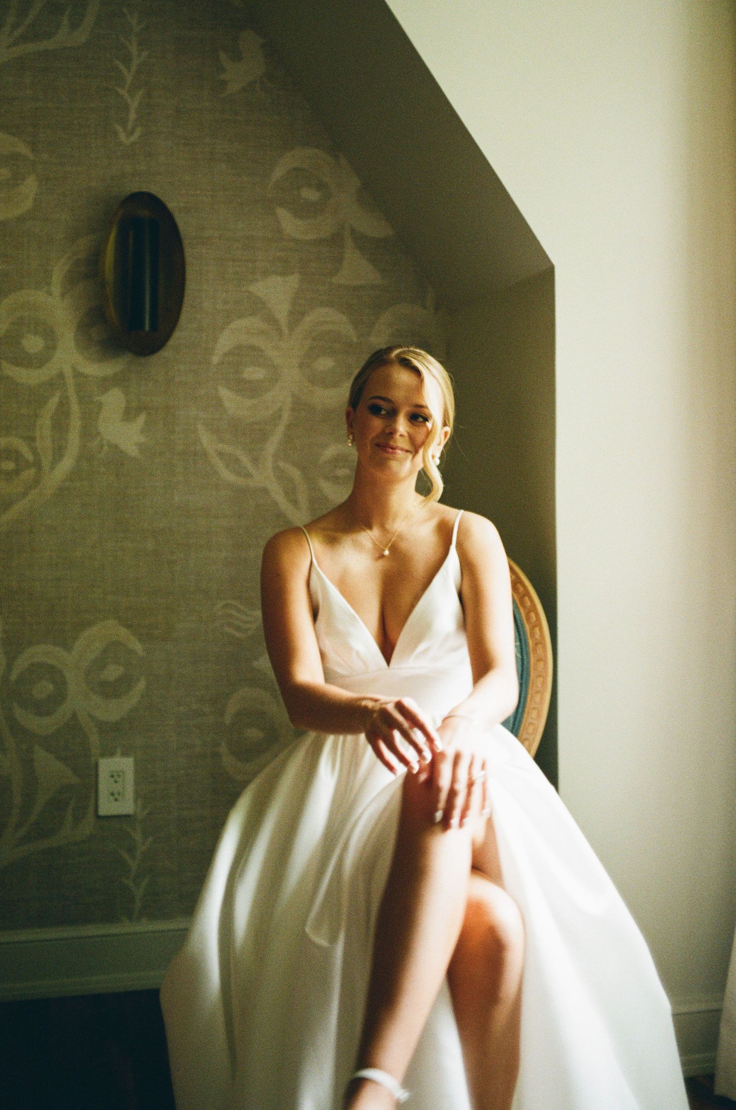 Elegant bridal portrait showing wedding dress details in room with patterned wallpaper.