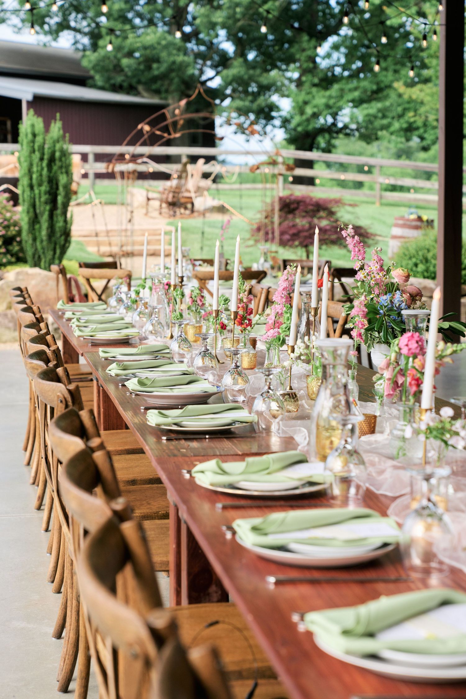 Elegantly set rustic outdoor wedding table with pink floral centerpieces and green accents.
