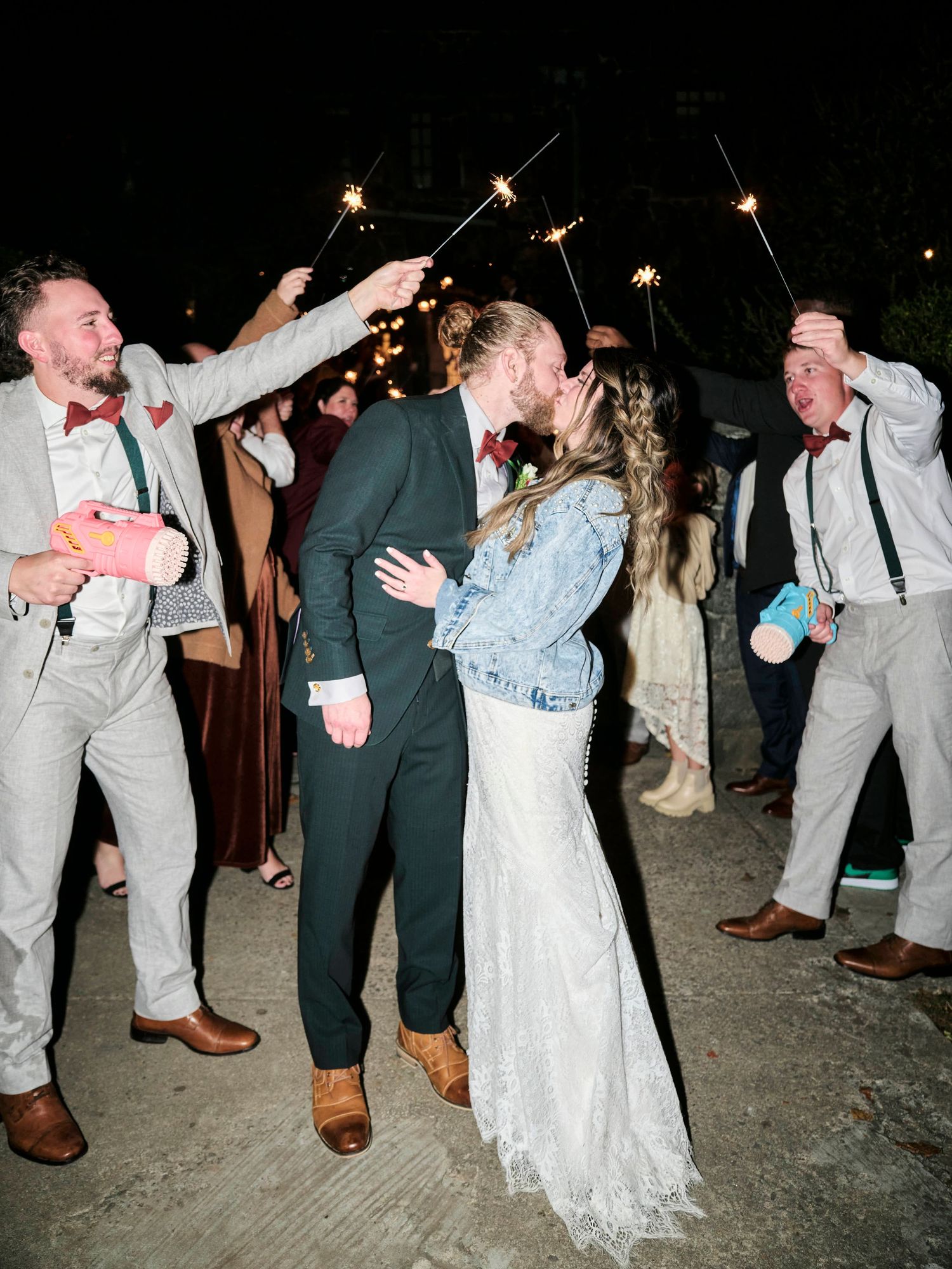 A couple shares a kiss during their sparkler exit while guests celebrate.