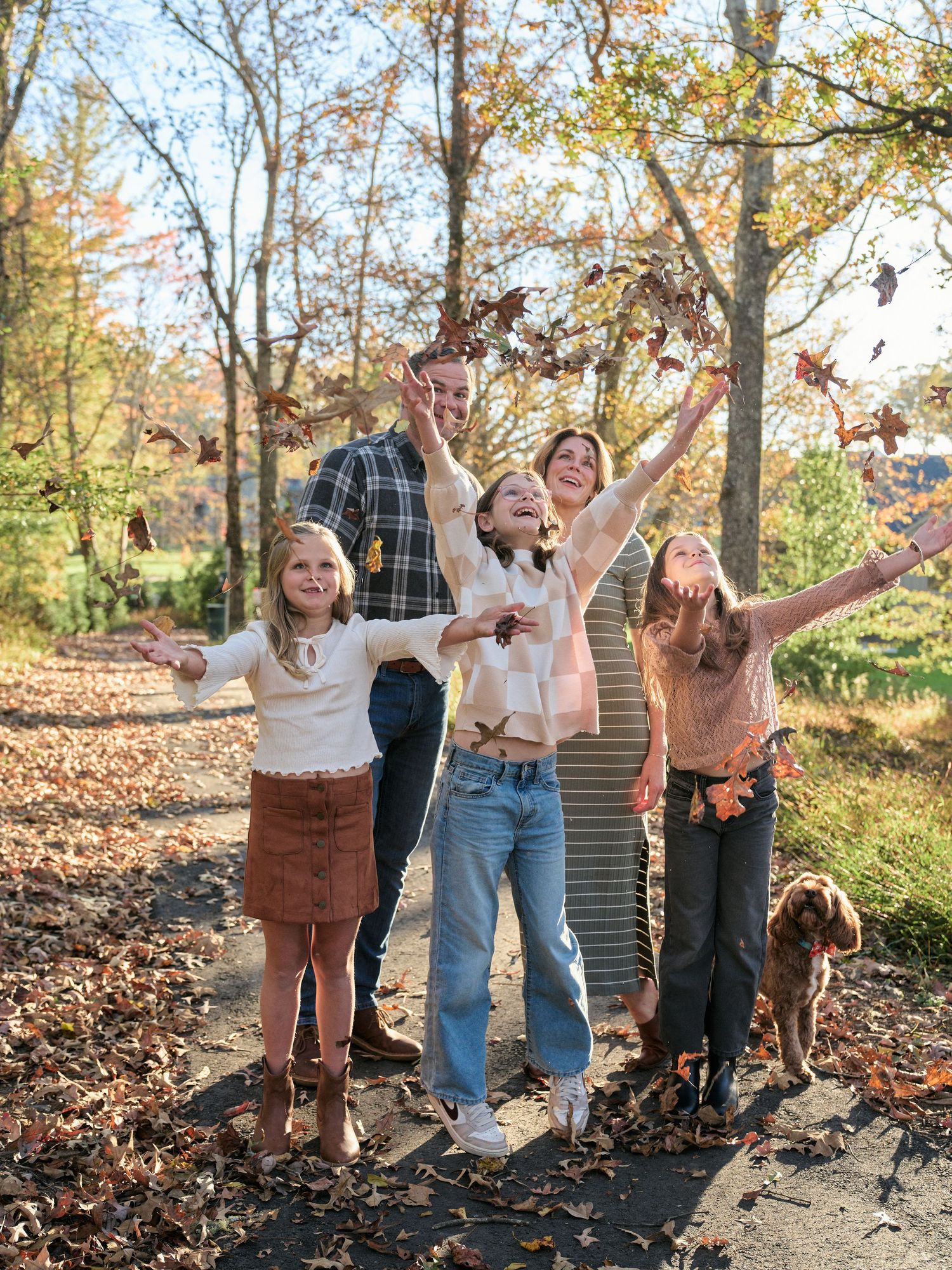 A joyful family plays together in a pile of autumn leaves on a sunny fall afternoon.