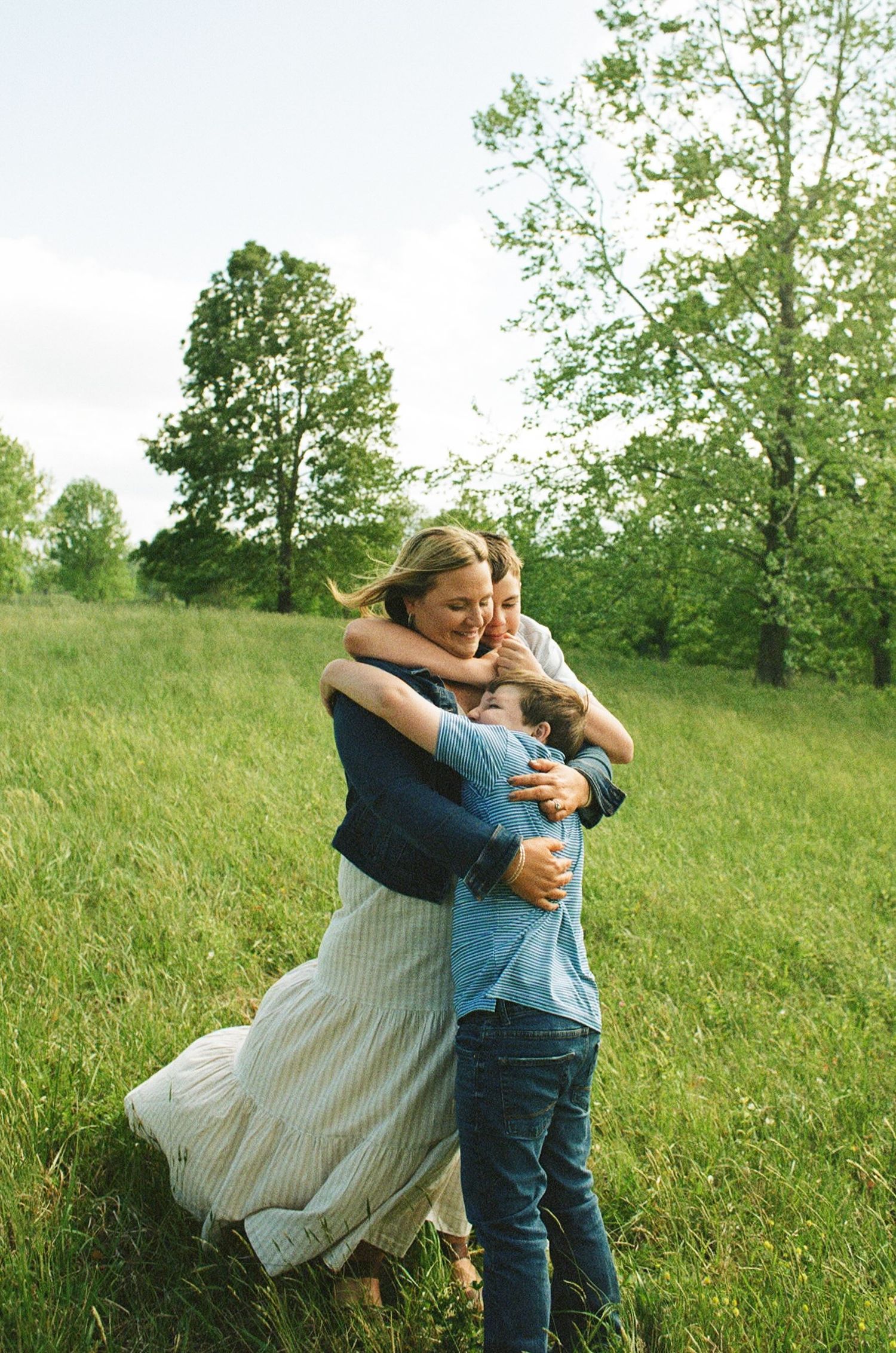A couple embraces joyfully in a lush green meadow, the woman in a striped dress lifting her leg as they hug.