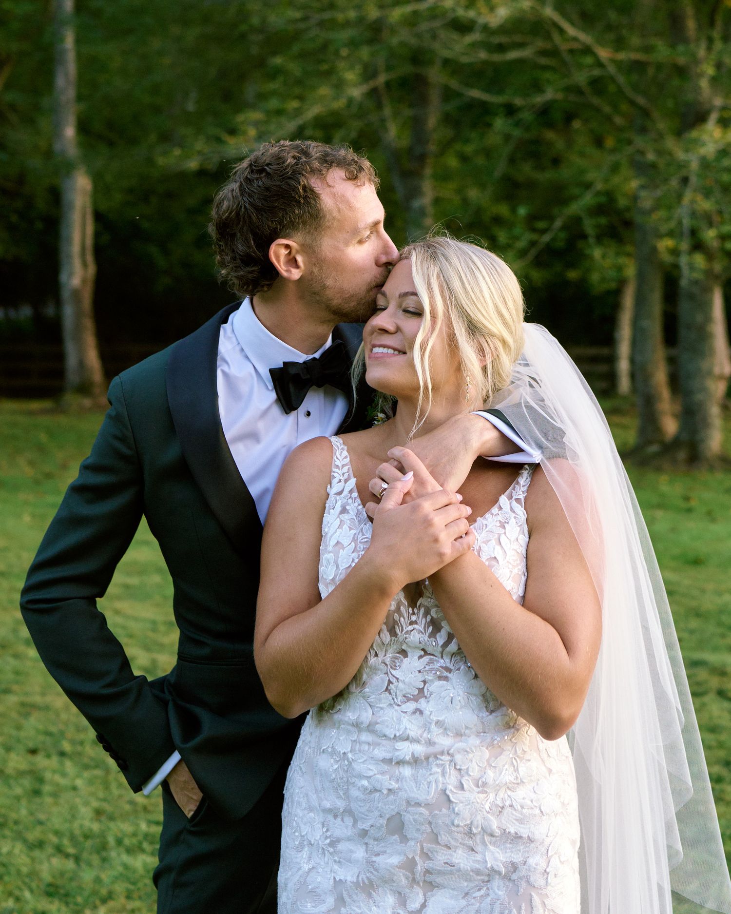 A couple shares an intimate moment during their outdoor wedding ceremony in a lush green forest setting.