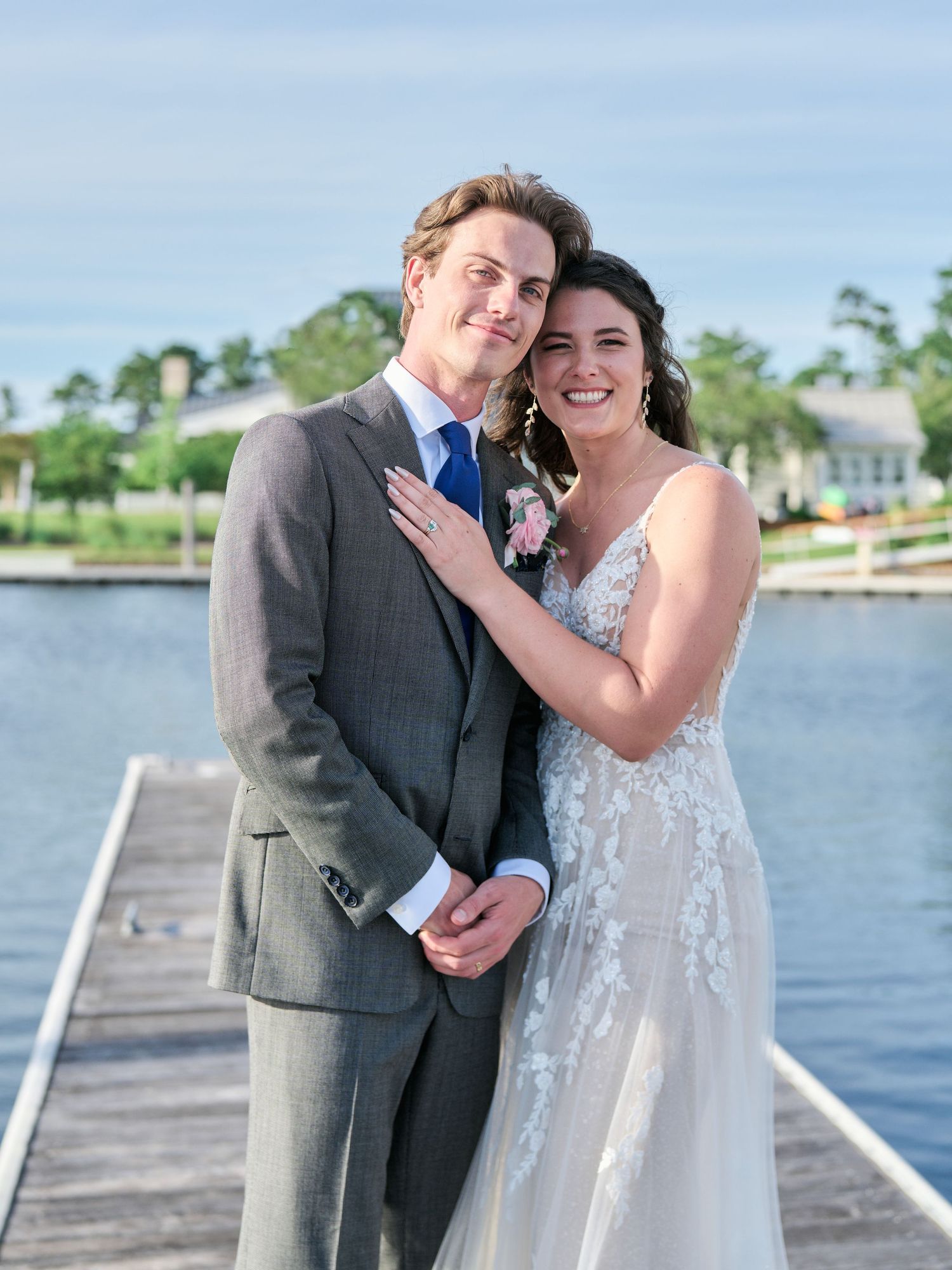 A couple in wedding attire poses together on a wooden dock by a lake on their special day.