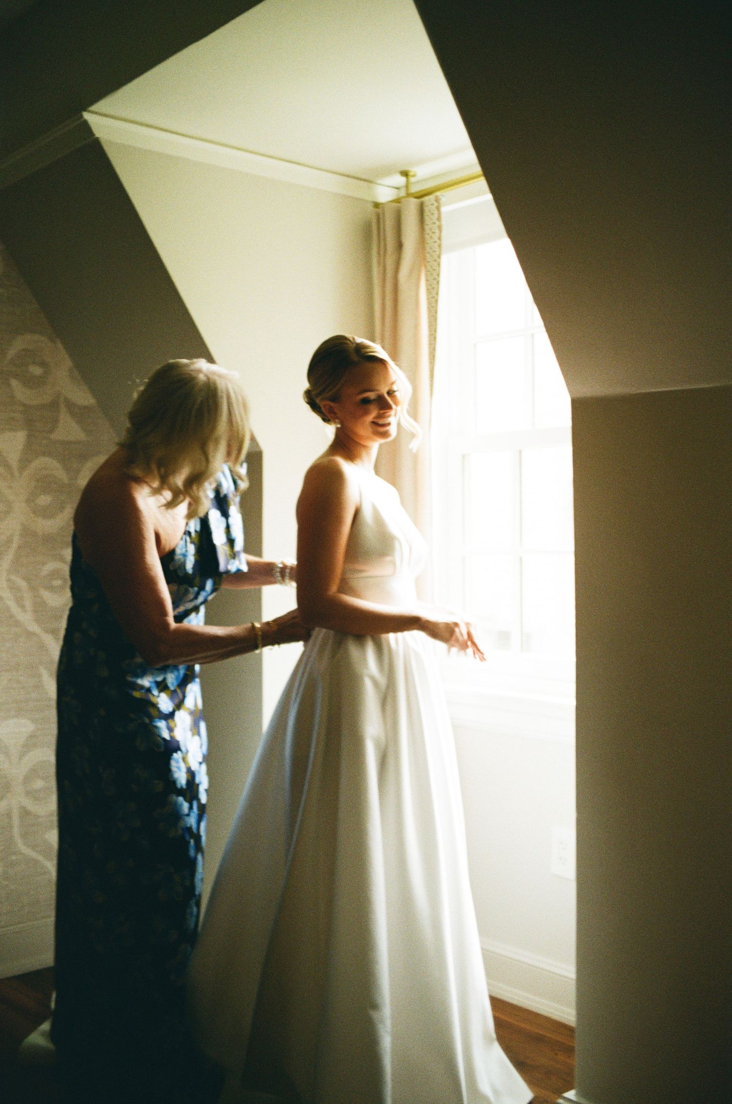 Intimate getting ready moment in sunlit room with wedding dress preparations.