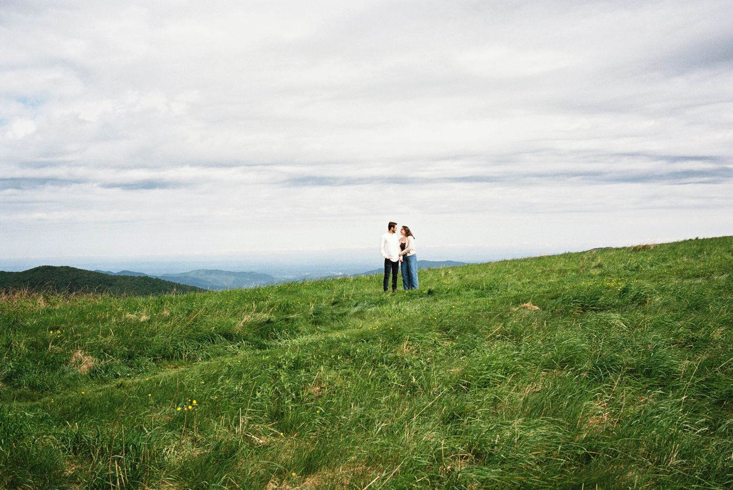 Hilltop wedding photos show figures silhouetted against a cloudy sky on grassy terrain.