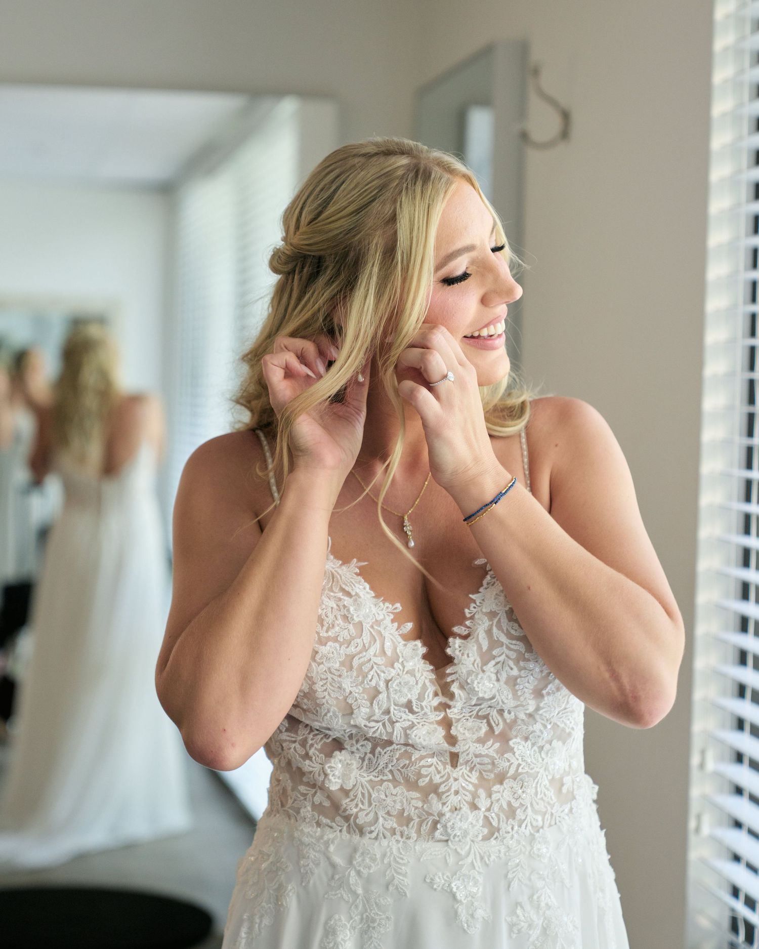 Getting ready moment captured in natural window light with bridal jewelry and lace details.