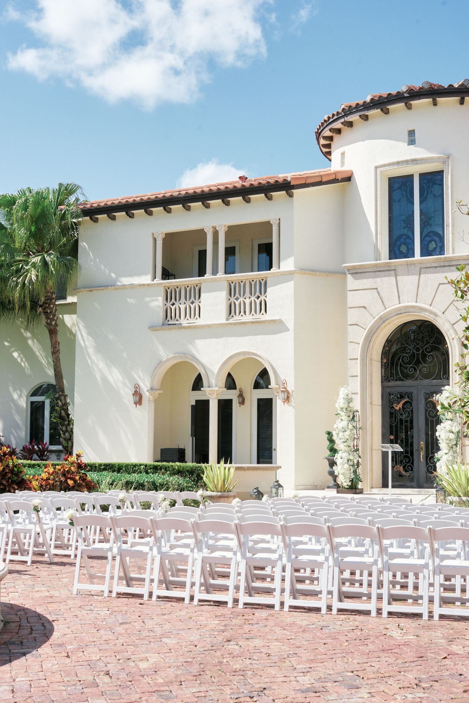 Elegant Mediterranean wedding venue with white chairs arranged on brick patio for outdoor ceremony.
