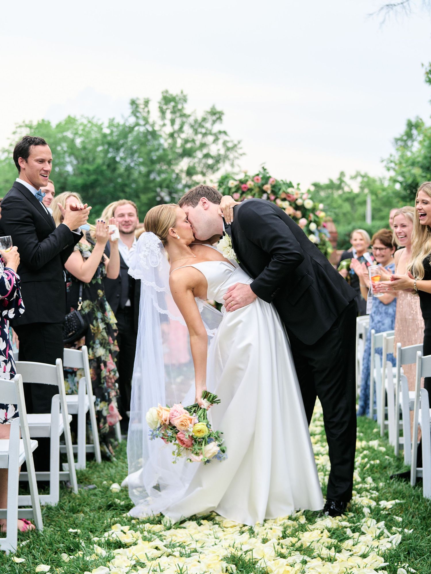 Wedding couple shares romantic moment on outdoor aisle surrounded by guests and floral decorations.