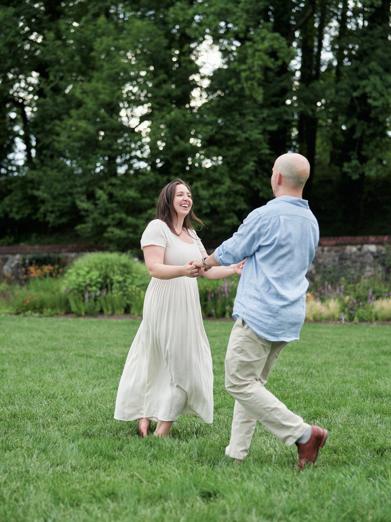 A couple dances joyfully on a lush green lawn with trees in the background.