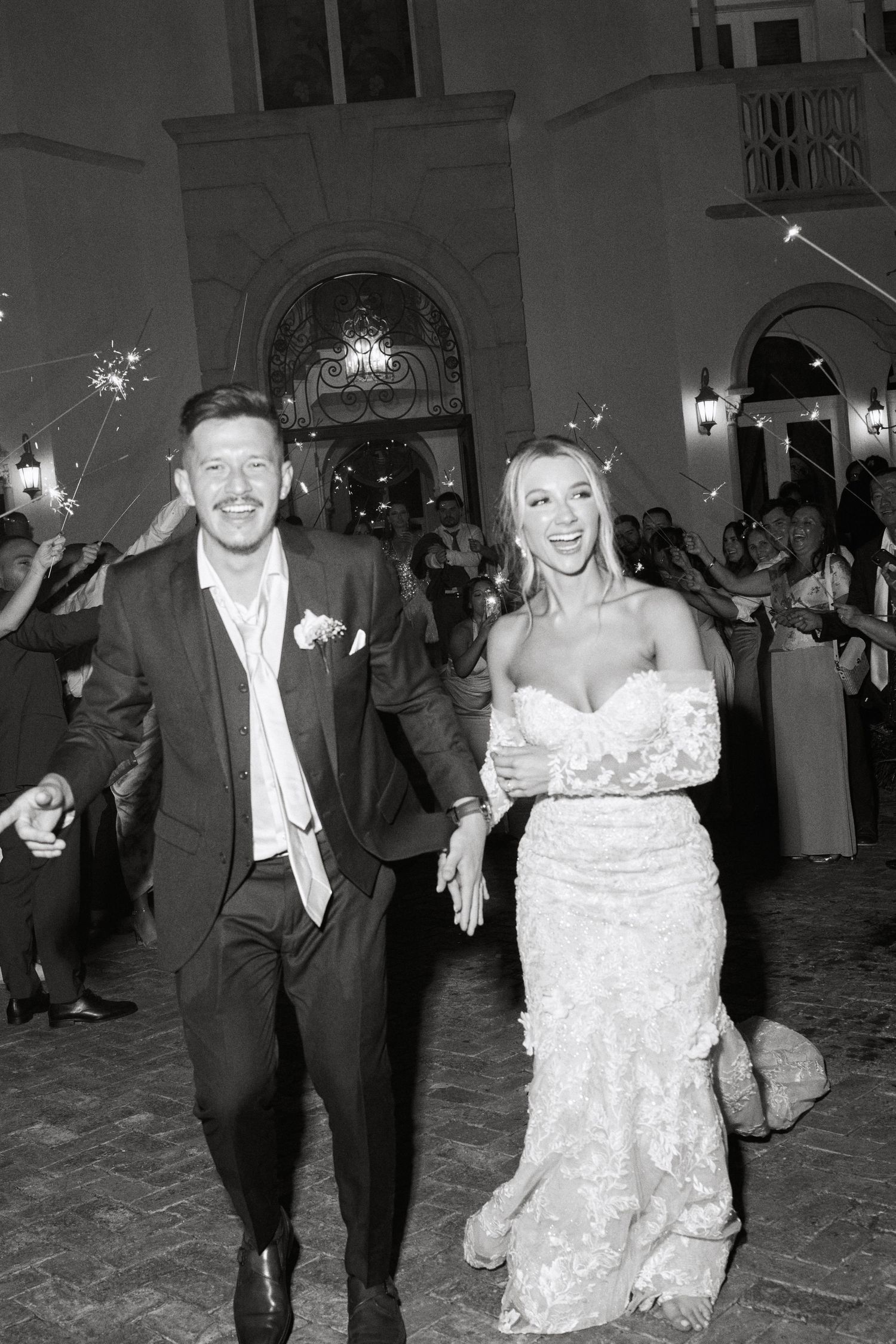 Black and white image of bride and groom celebrating during sparkler exit at wedding.