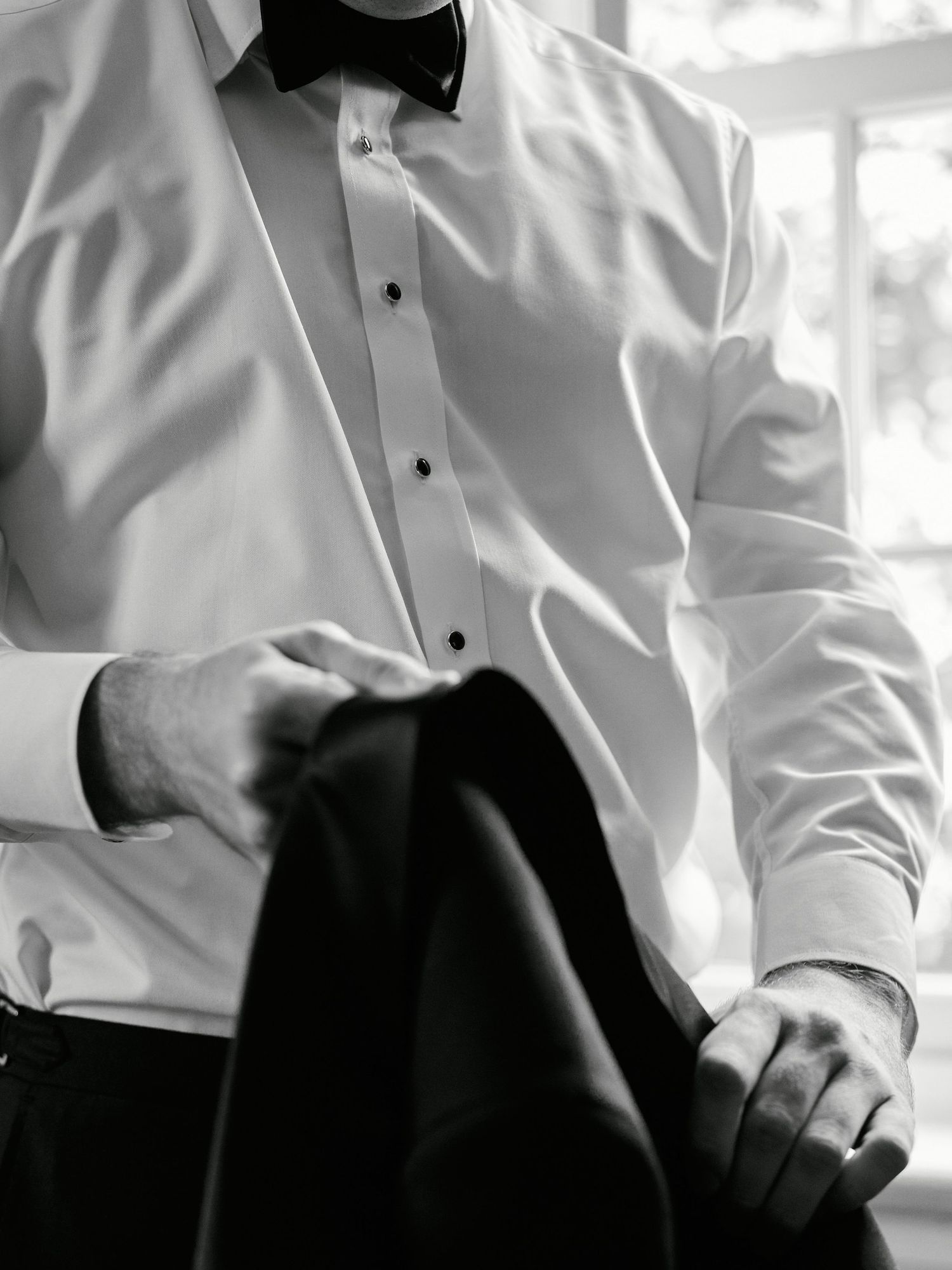 Close-up detail of white tuxedo shirt and black bow tie being adjusted.