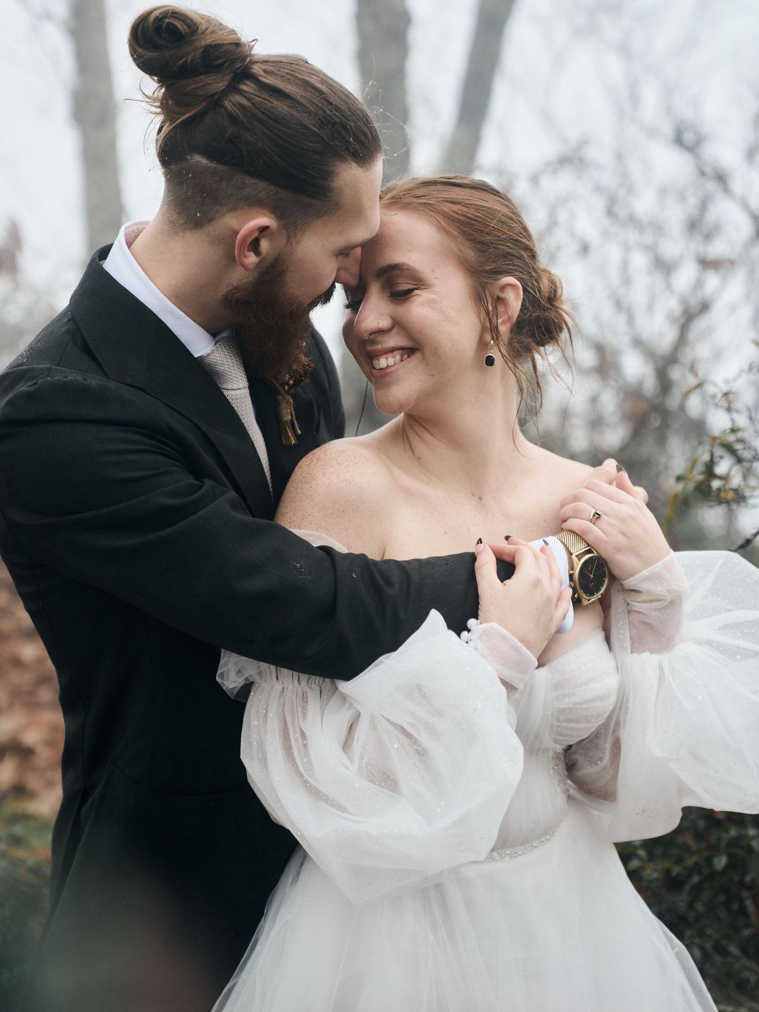An intimate wedding portrait showing tender embrace against a foggy forest backdrop.