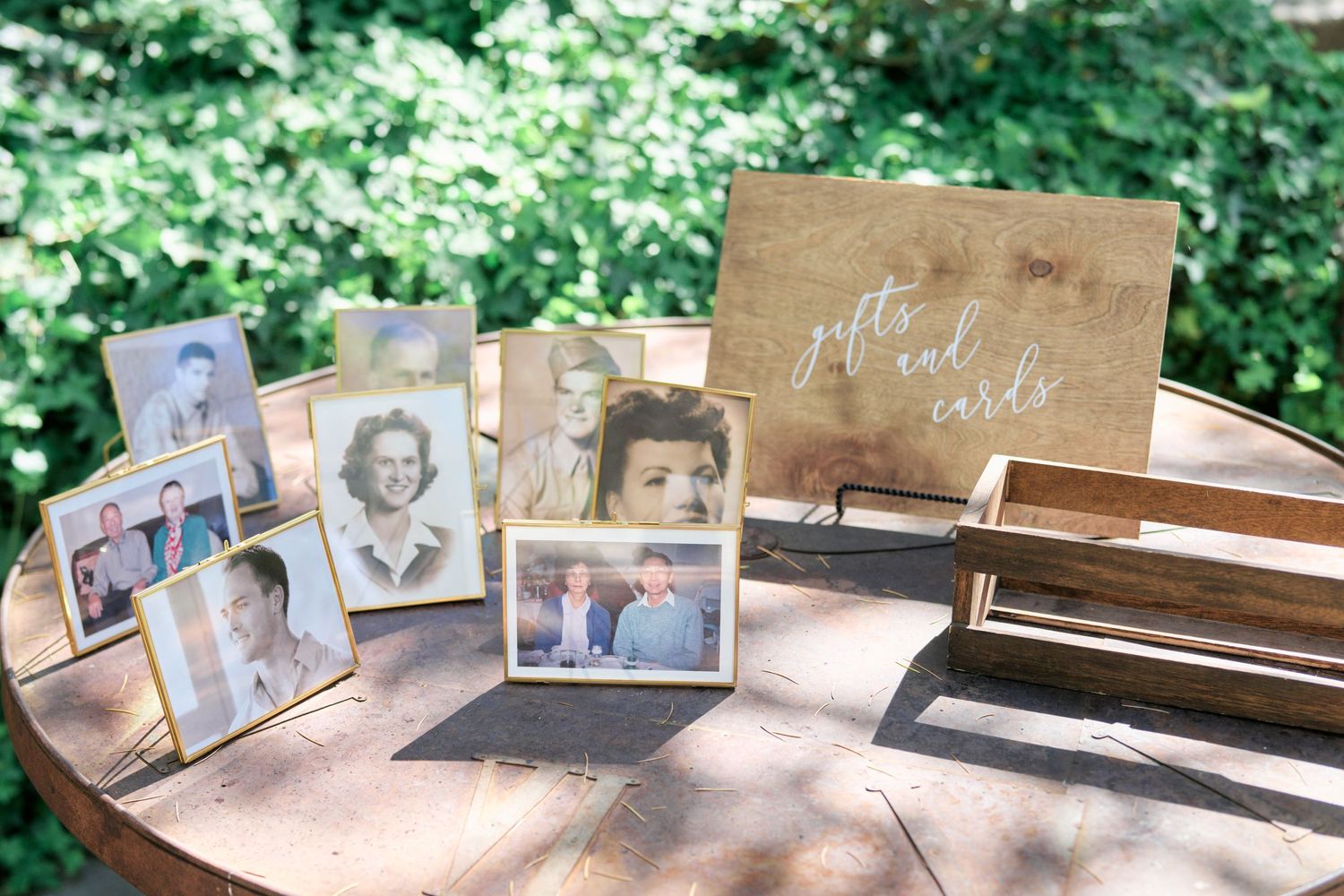 Vintage photographs displayed on a wooden table with a rustic sign in an outdoor setting.