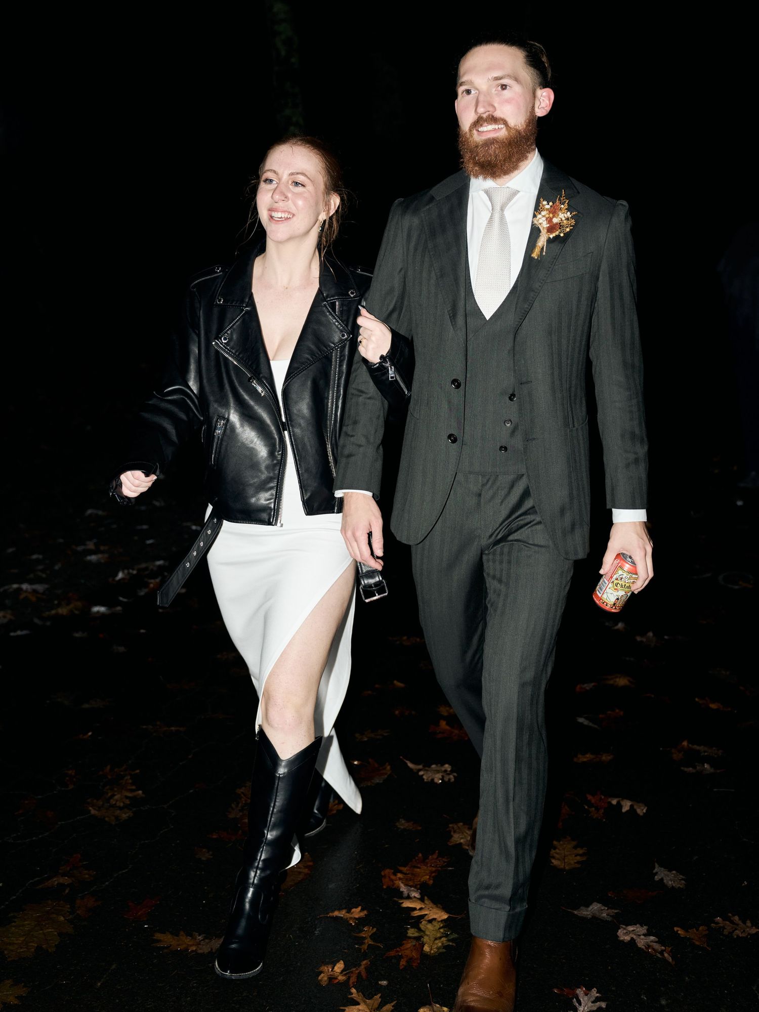 A couple walks together at night, with the bride wearing a leather jacket over her white dress.