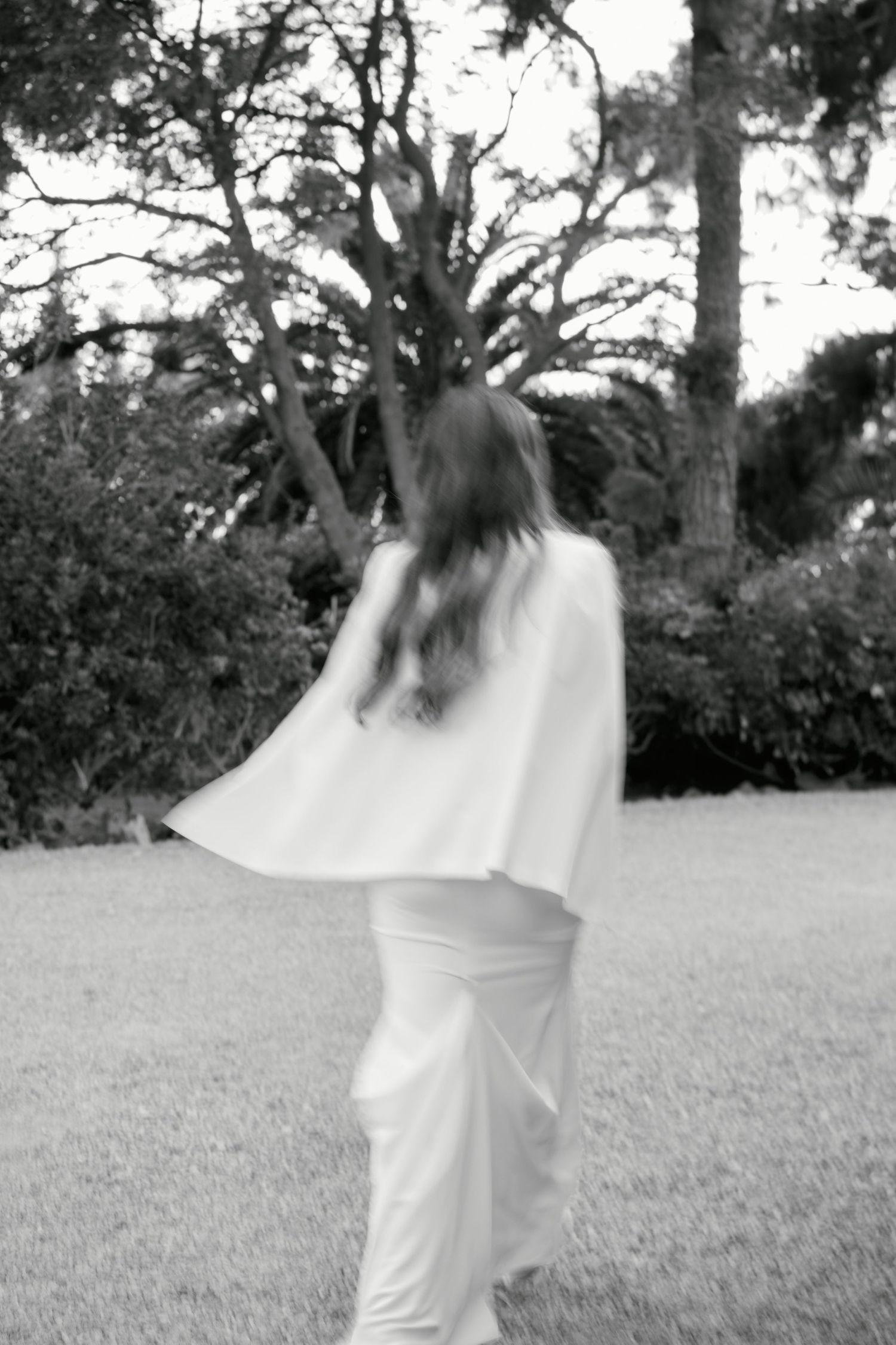 Black and white photo of flowing white dress movement in an outdoor garden setting.