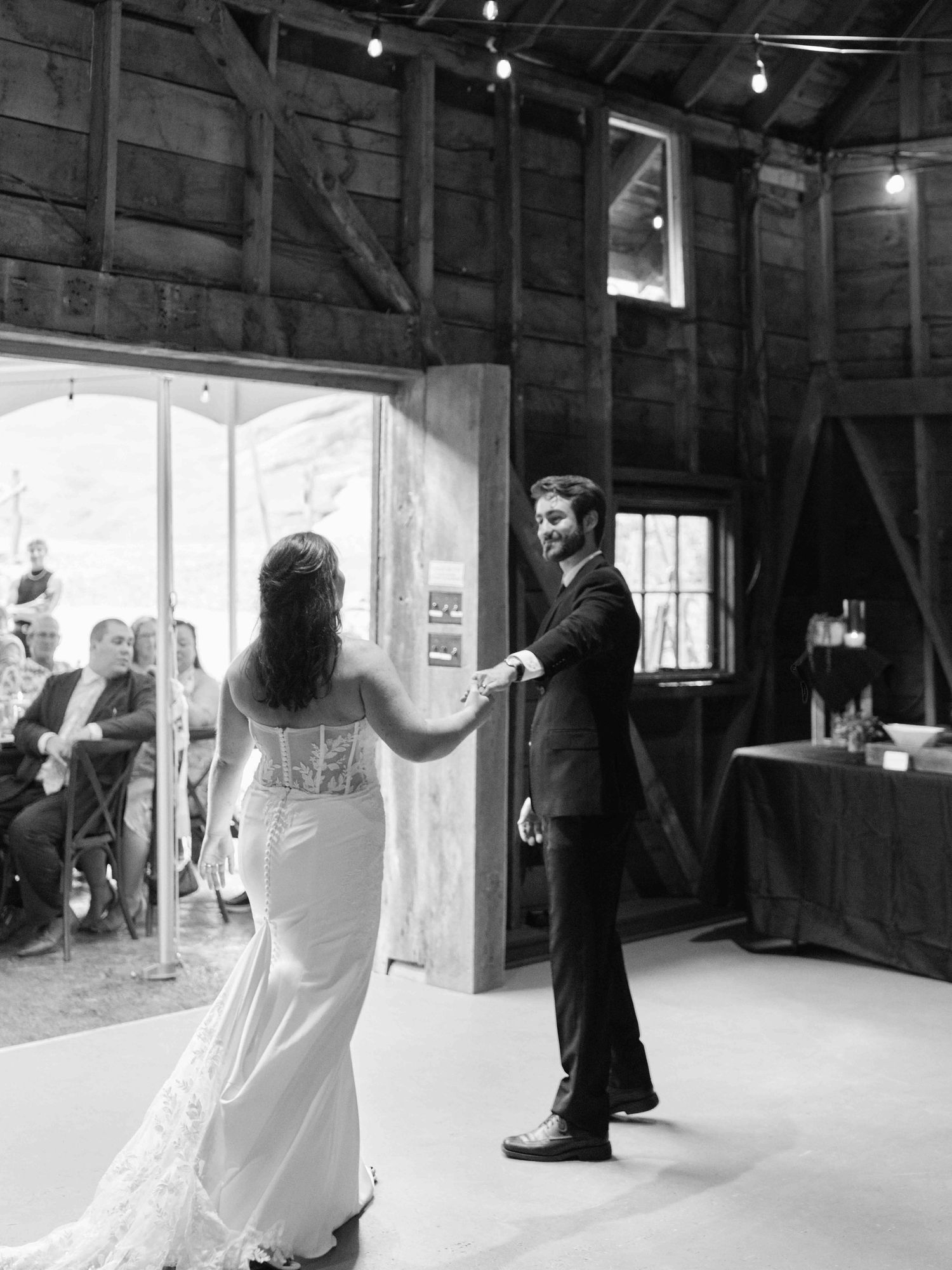 Black and white photo of bride and groom sharing first dance in rustic barn wedding venue.