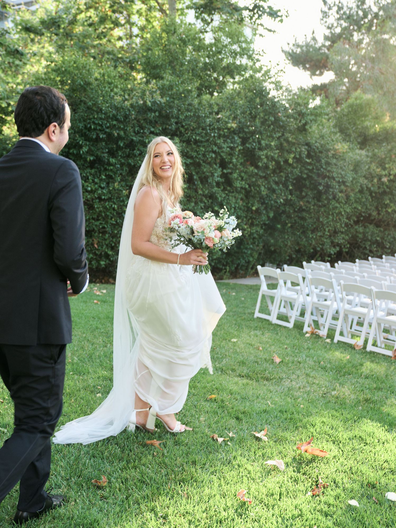 Garden wedding scene with white chairs and couple on green lawn.