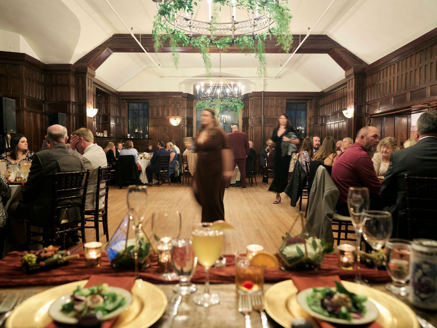 Wedding reception in a grand wood-paneled hall with chandelier and table settings.