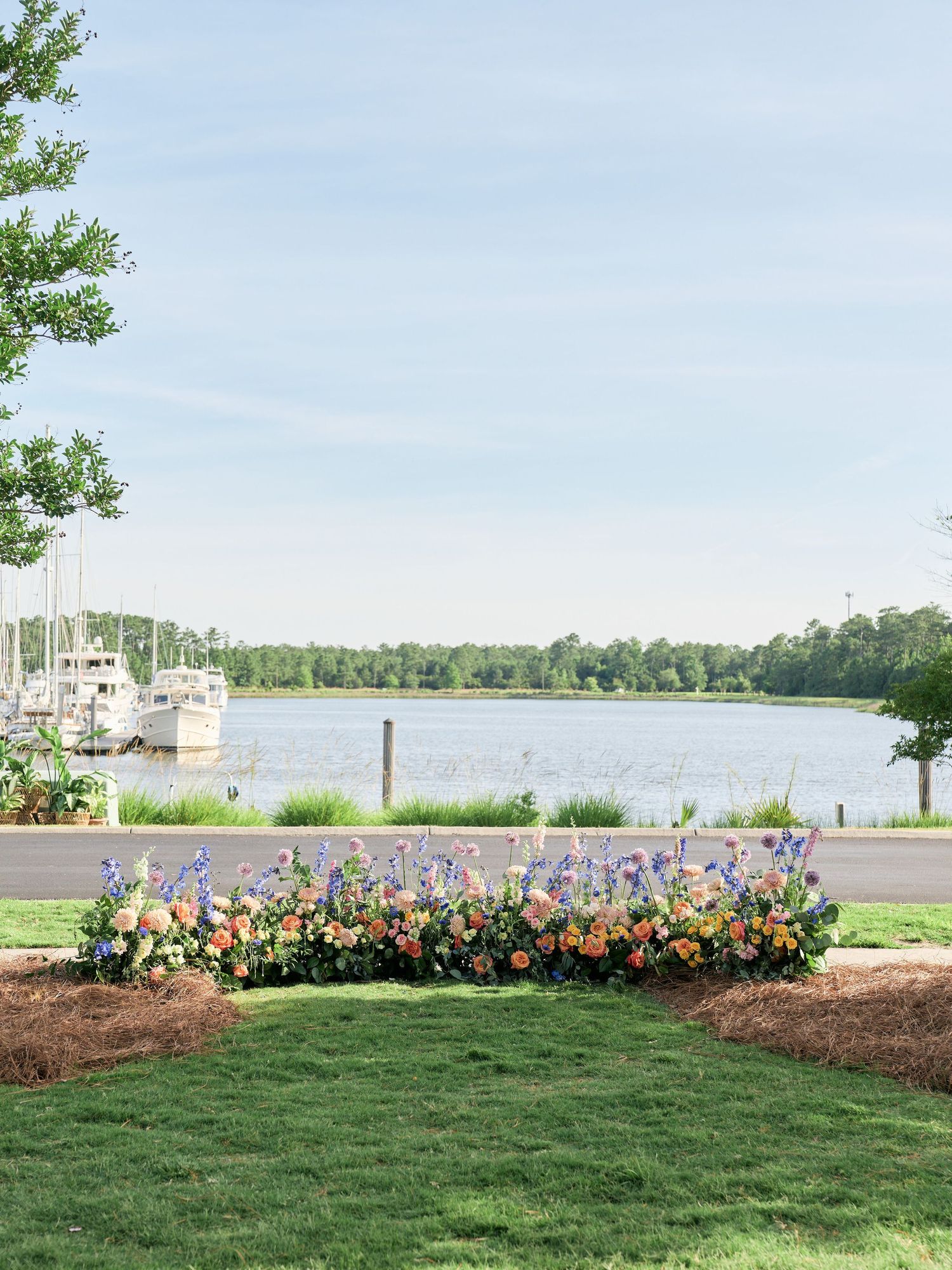Colorful flower bed with sailboats docked along a peaceful waterfront marina on a sunny summer day.