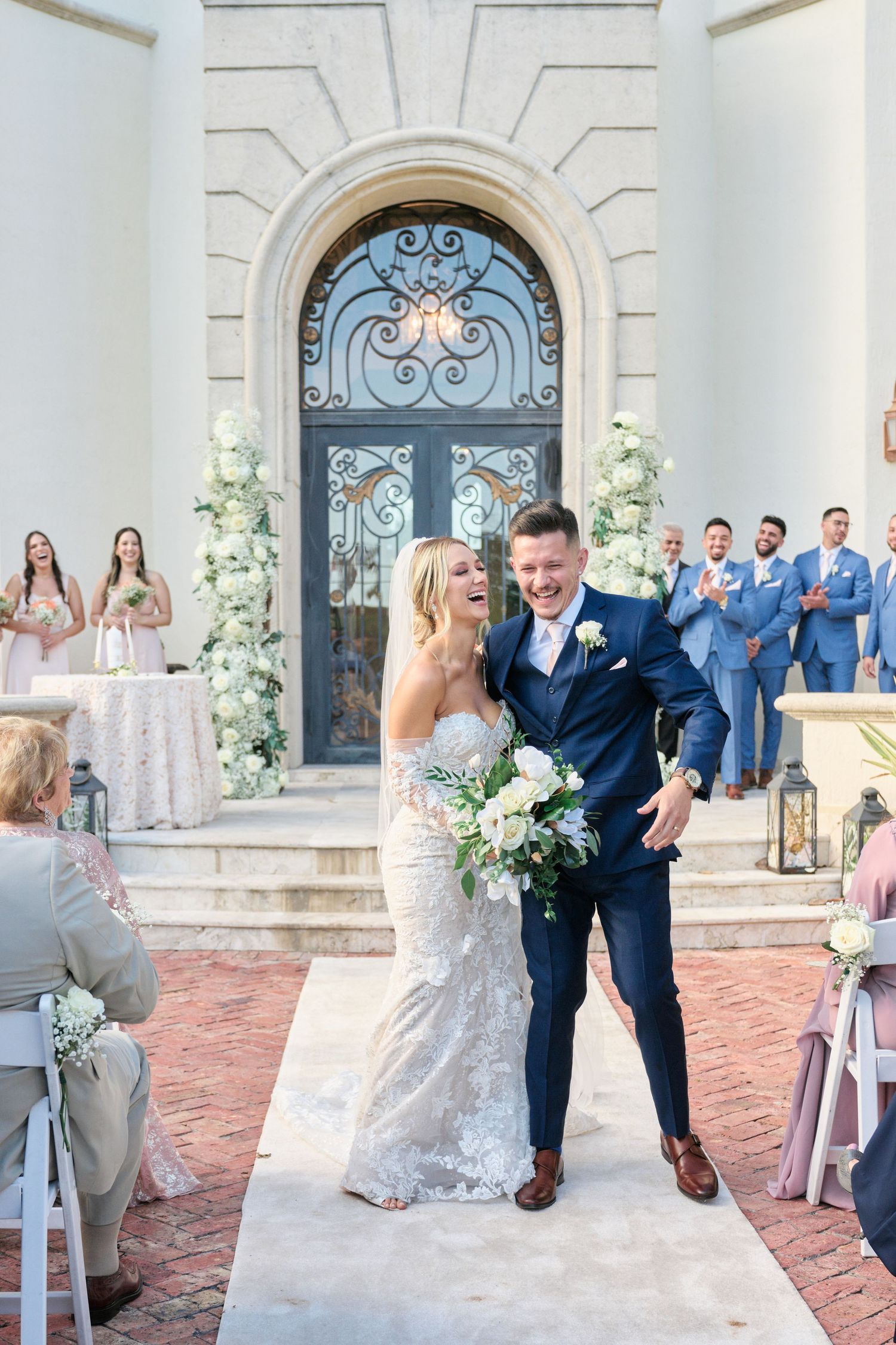 Newlyweds celebrate outside ornate church entrance with wedding party in blue suits.