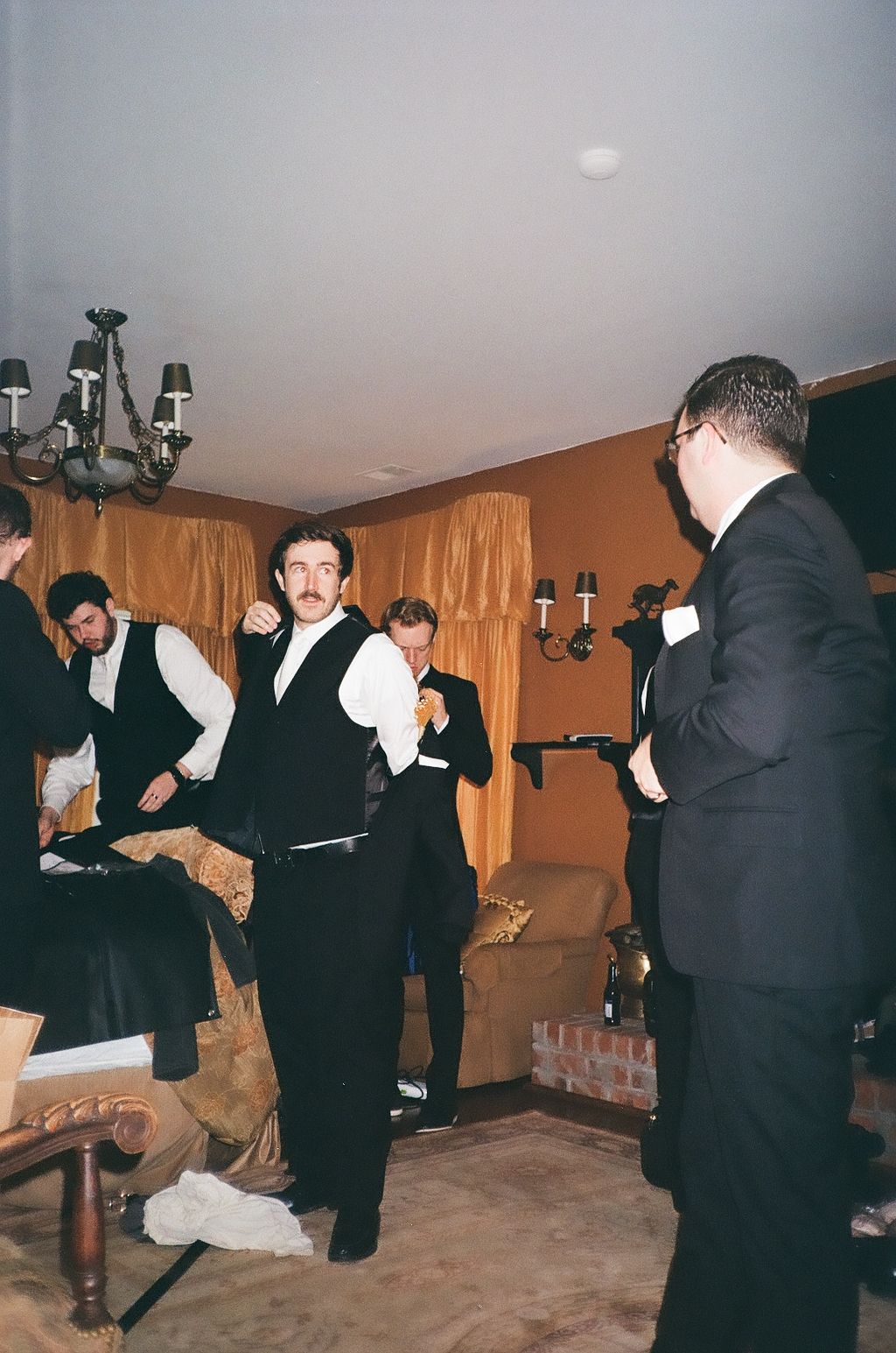 Groomsmen in formal black suits and bowties gather in a dimly lit room during wedding preparations.