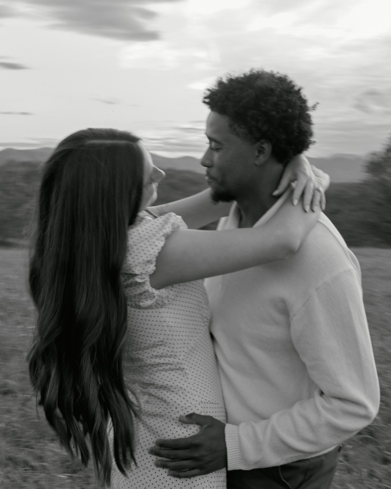 A couple embraces while standing outdoors in black and white photography.