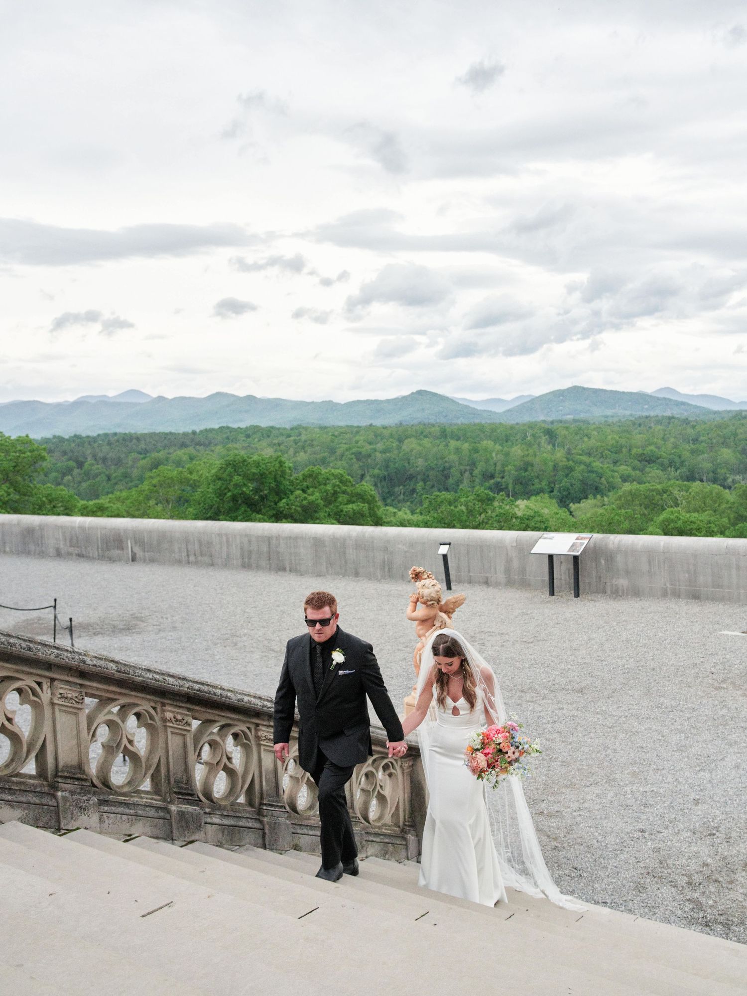 A wedding couple poses along a stone balcony overlooking scenic mountain views at the Biltmore Estate in Asheville.