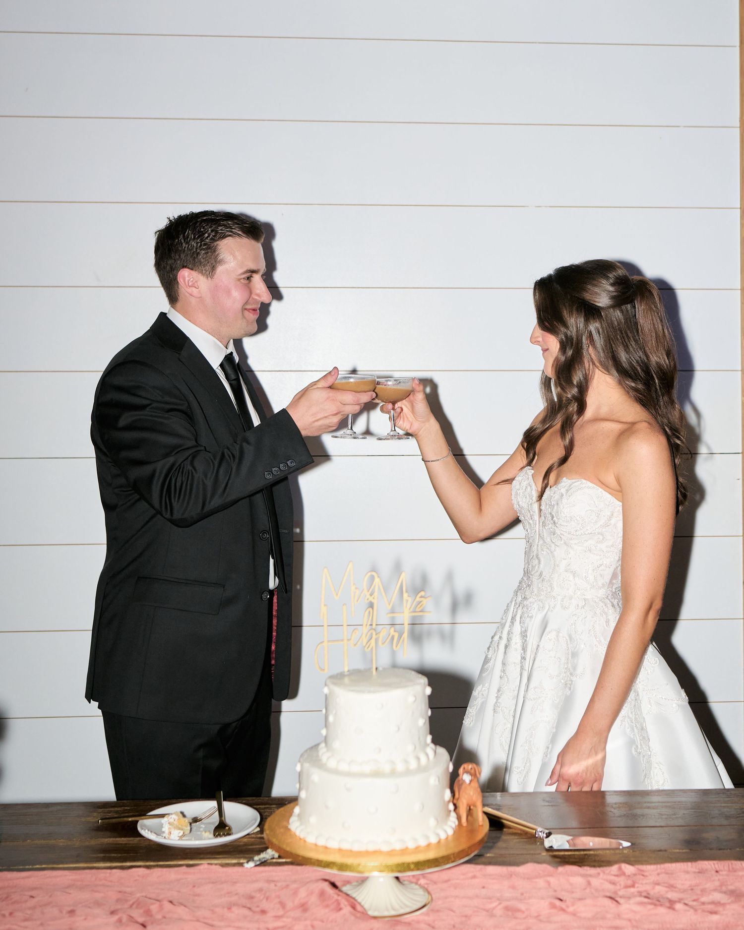 Bride and groom toasting with champagne glasses over a white two-tier wedding cake at their reception.
