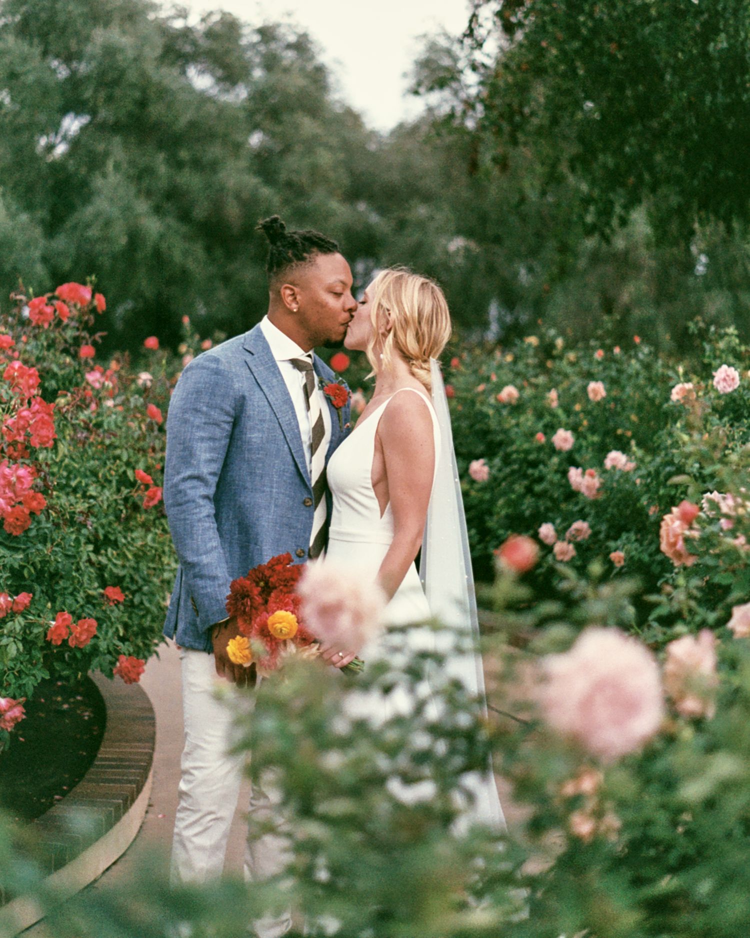 A romantic moment captured in a lush rose garden with blooming pink and red flowers creating a dreamy atmosphere.