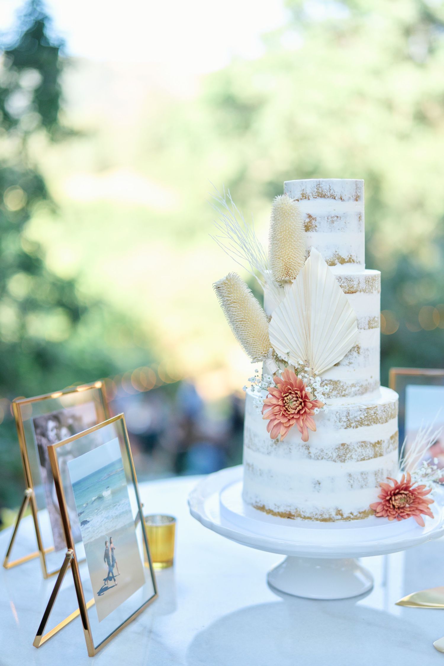 Semi-naked wedding cake decorated with dried flowers and pampas grass on a white cake stand.