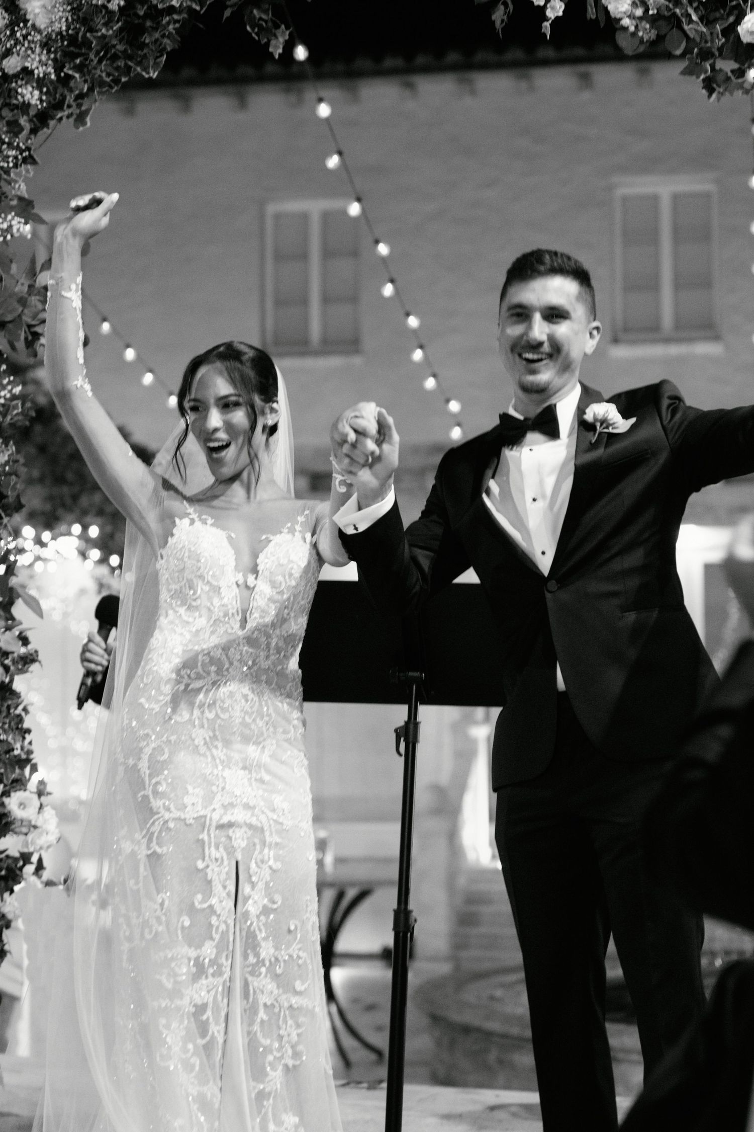 Joyous newlyweds celebrating with raised hands during outdoor wedding ceremony.