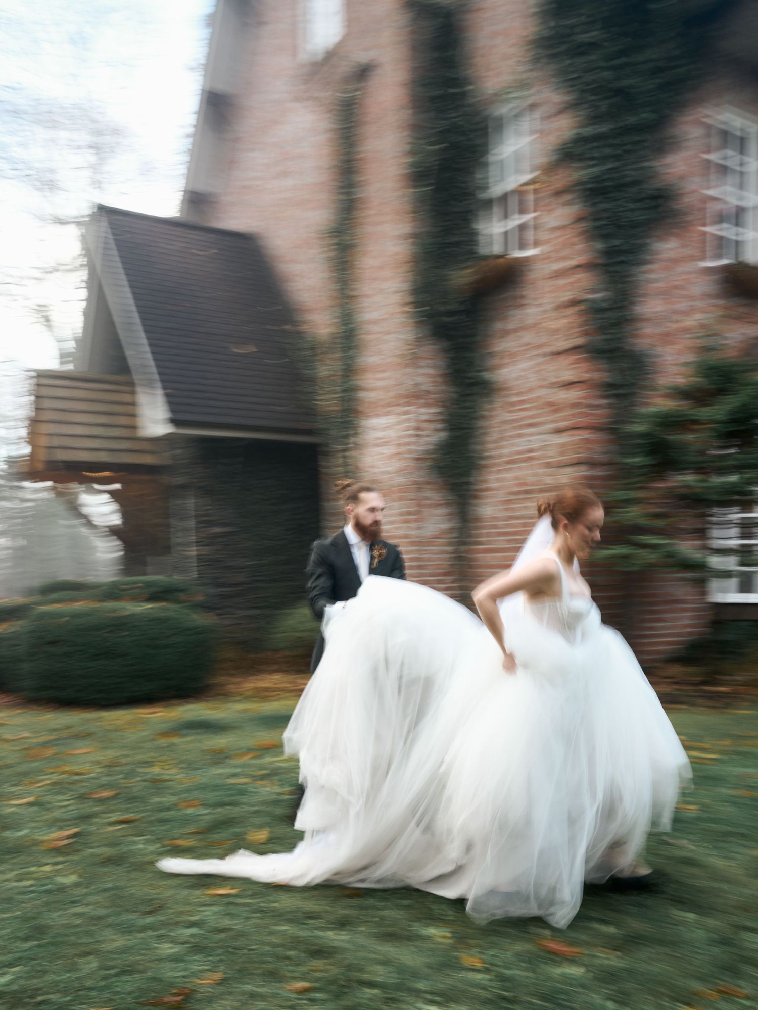 A wedding couple runs playfully outside a brick building on their special day.